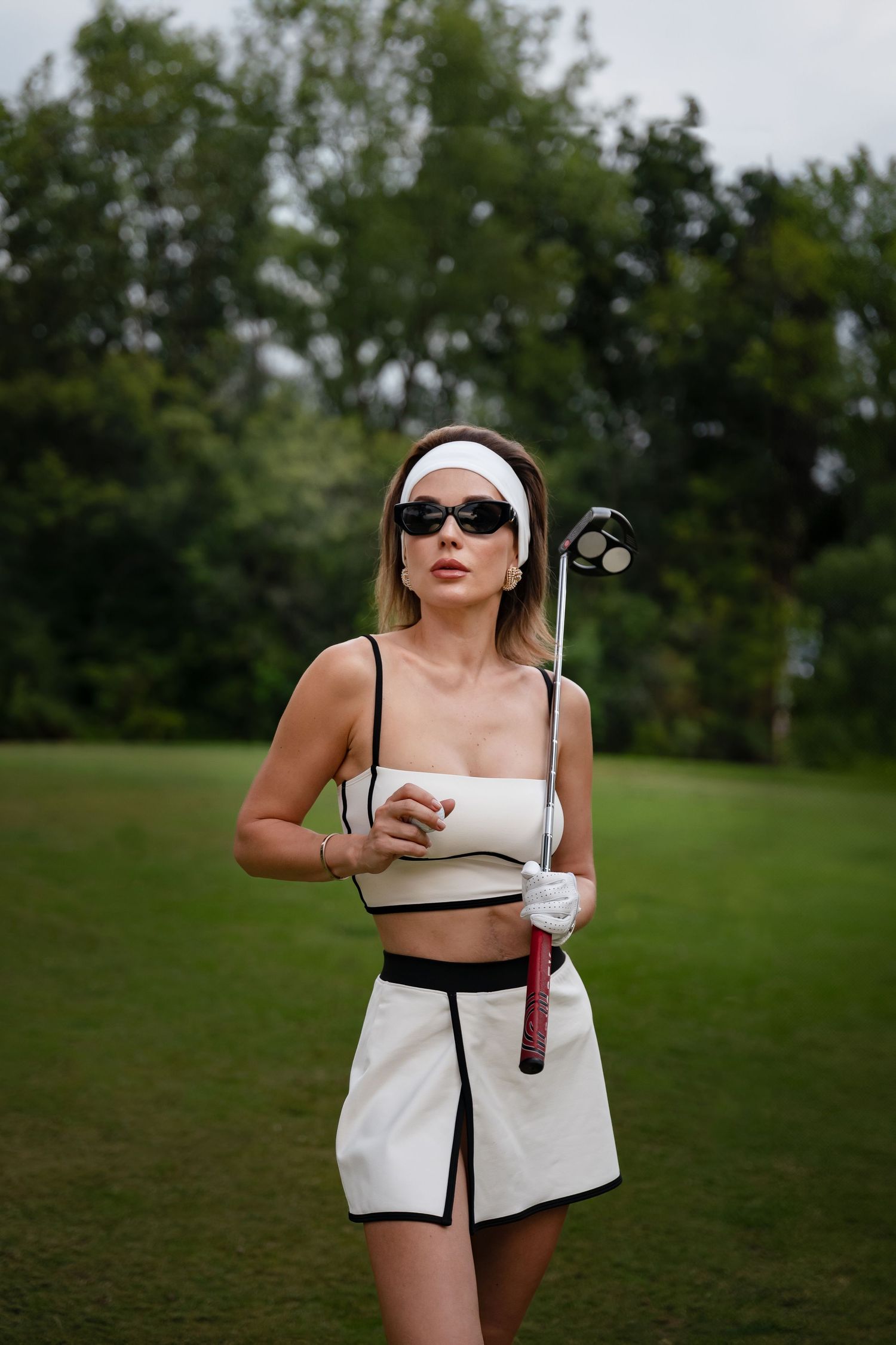 Sporty golfer in white crop top and skirt outfit holding club on course.