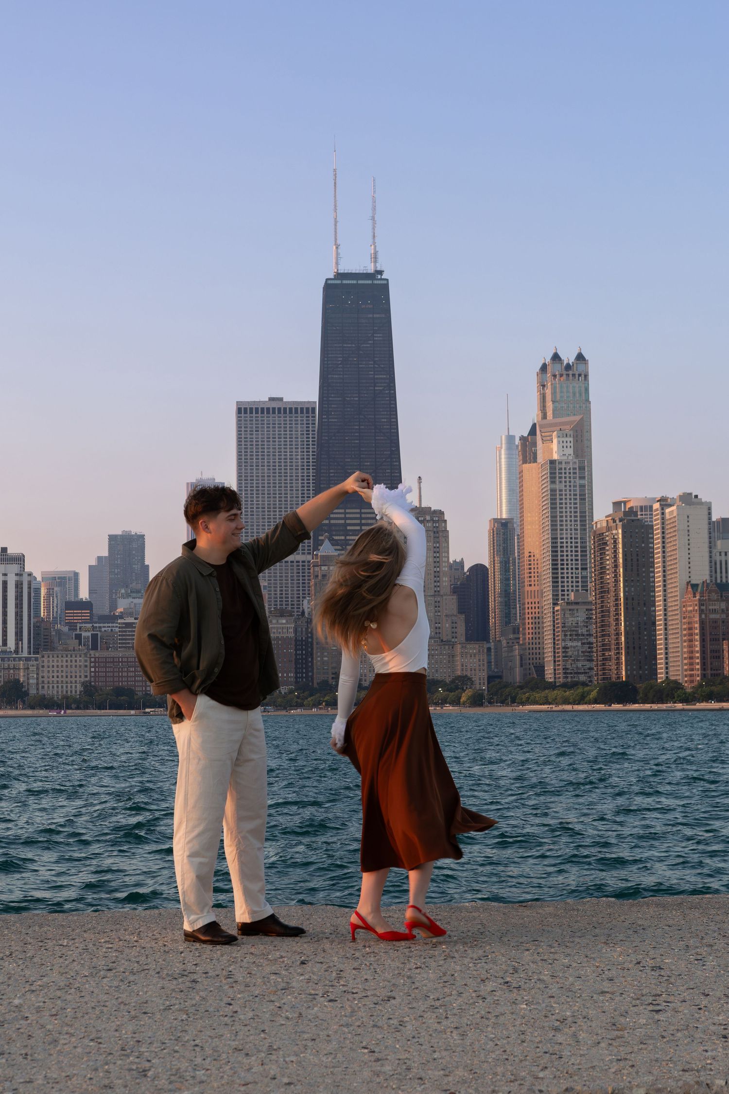 Two people strike playful poses on a beach with Chicago's iconic skyline and Lake Michigan in the background.