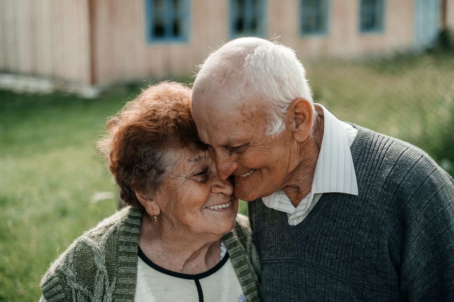 Intimate moment showing two elderly people sharing a tender embrace outdoors.
