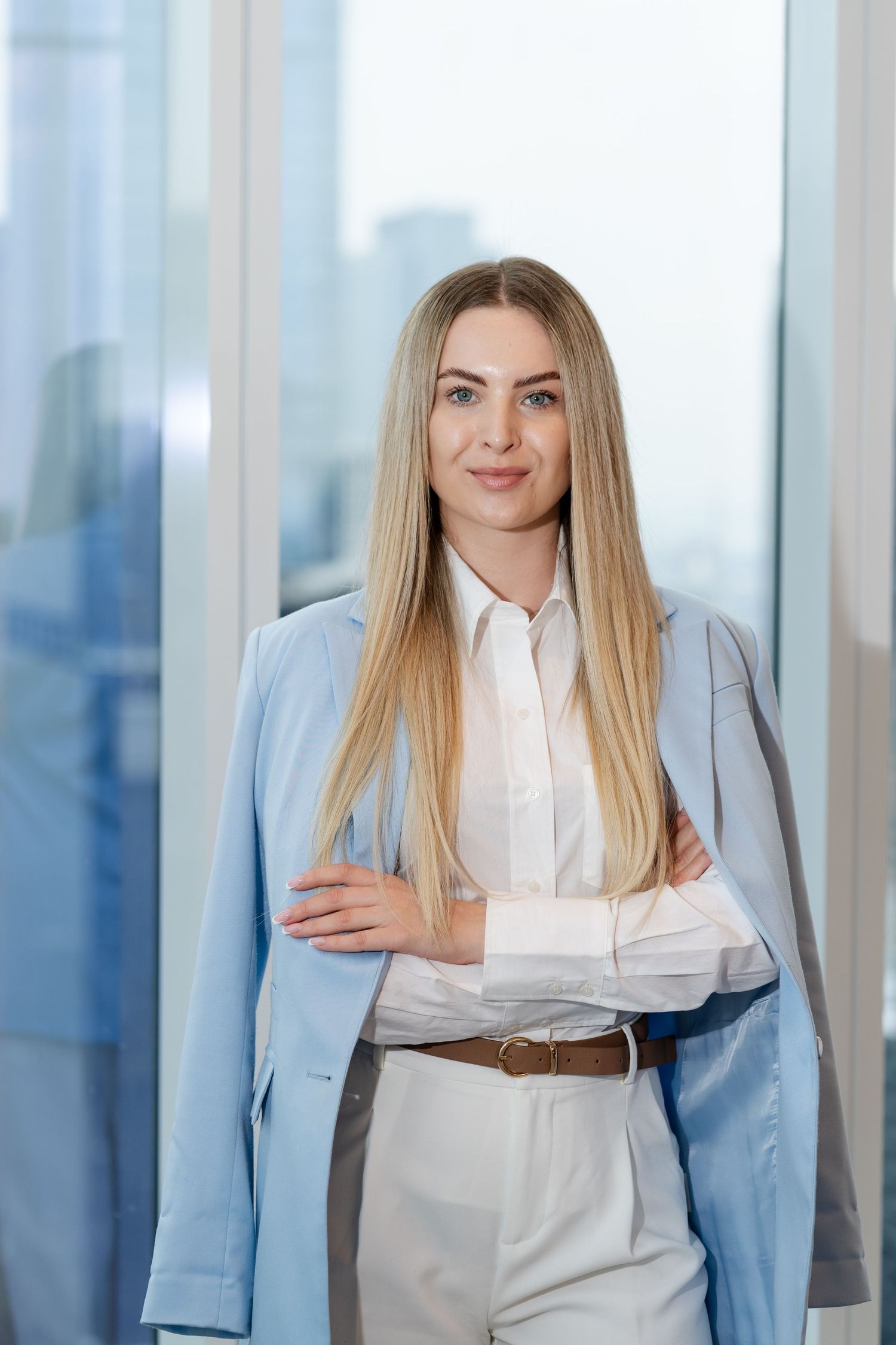 Professional in light blue blazer and white outfit poses in modern office.