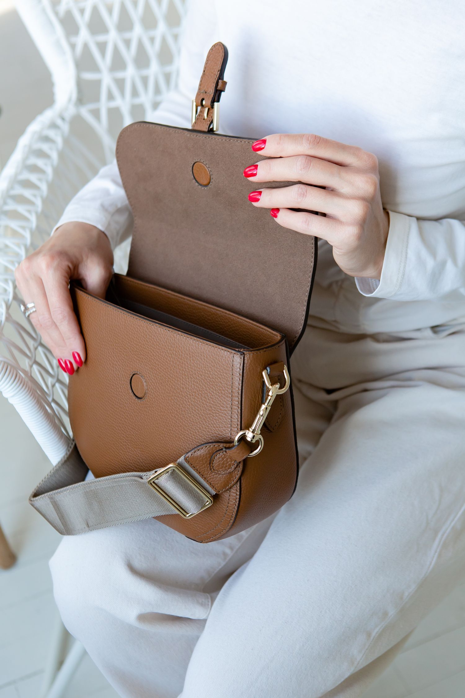 Brown leather crossbody bag with gold hardware being opened to reveal interior compartments.