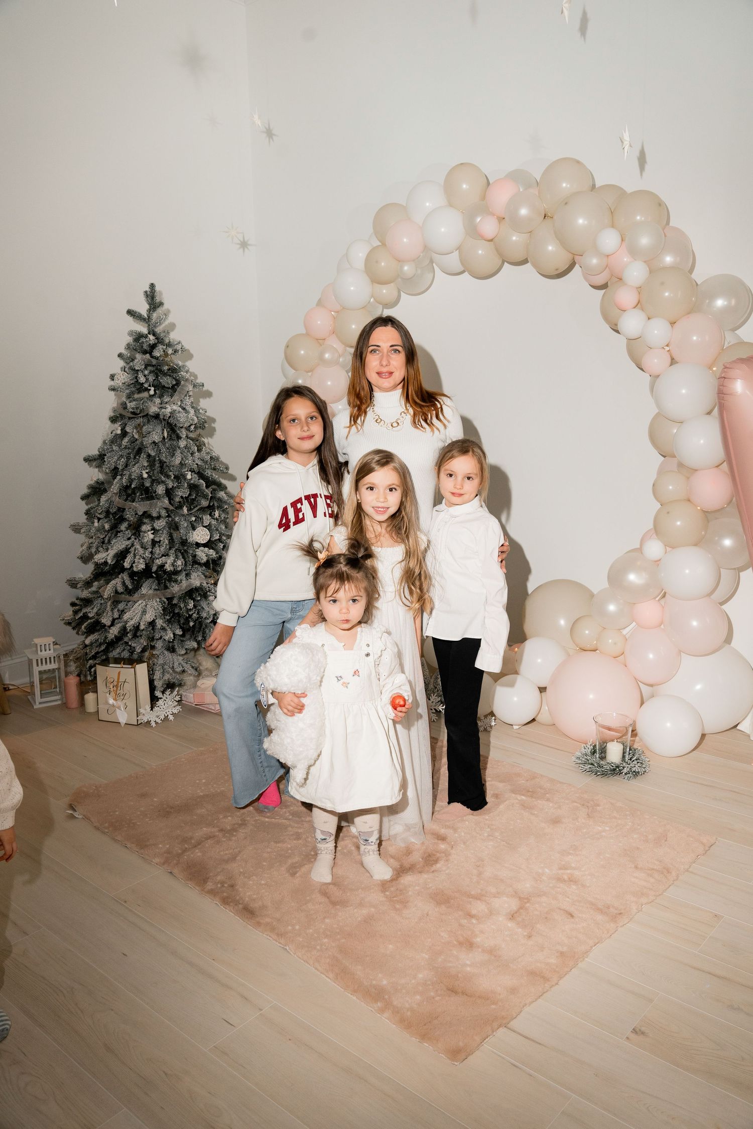 Family portrait under a pink and white balloon arch with a decorated Christmas tree in the background.