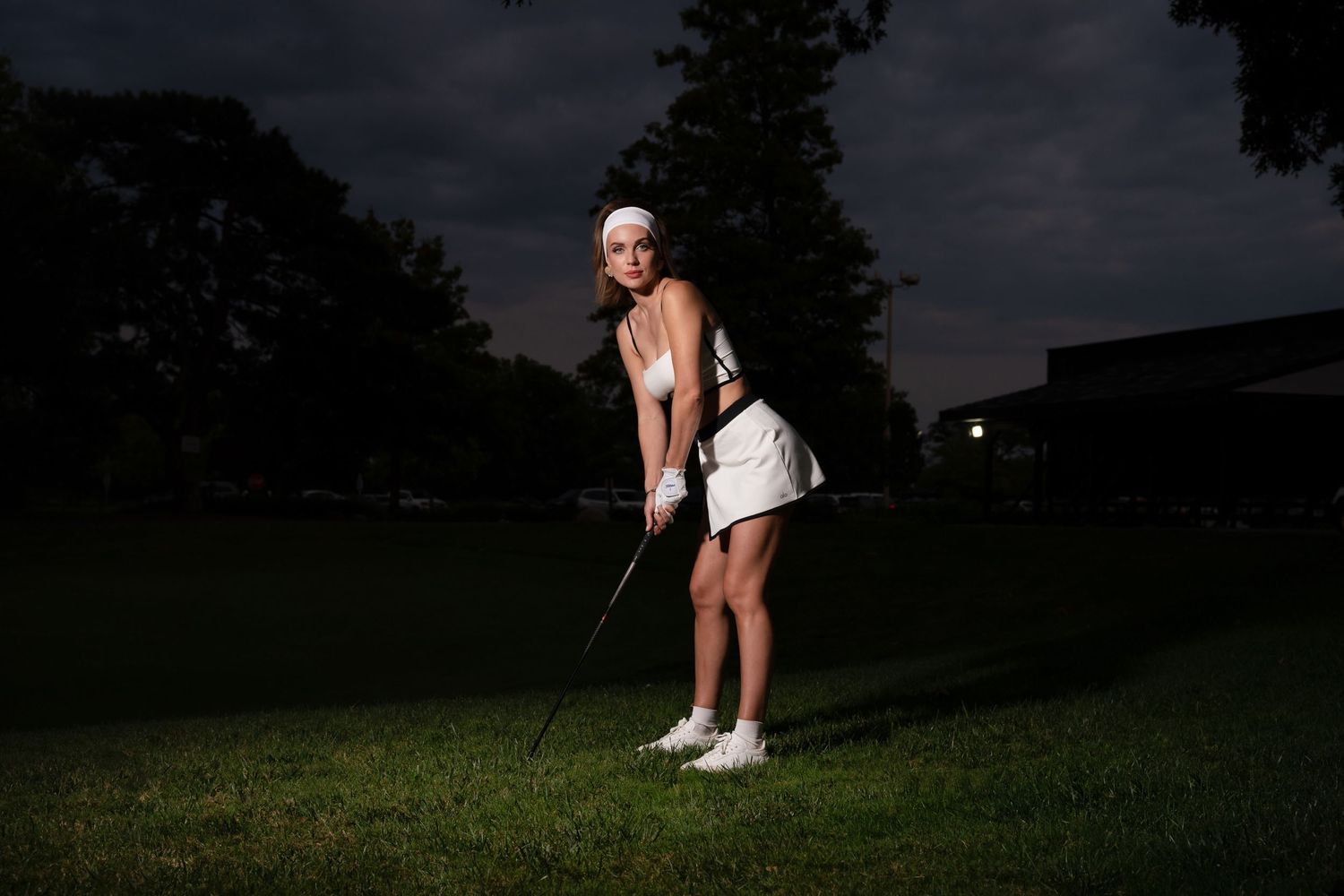 Person practicing golf swing at dusk on dark grassy field.
