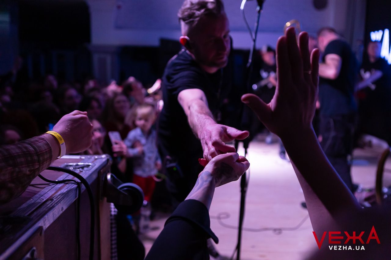 Concert performers reach out to touch hands with audience members during an energetic live show.