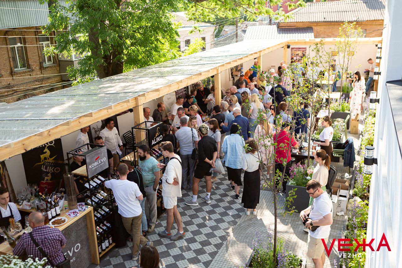Aerial view of a crowded outdoor wine tasting event with vendors and customers under covered pavilions.