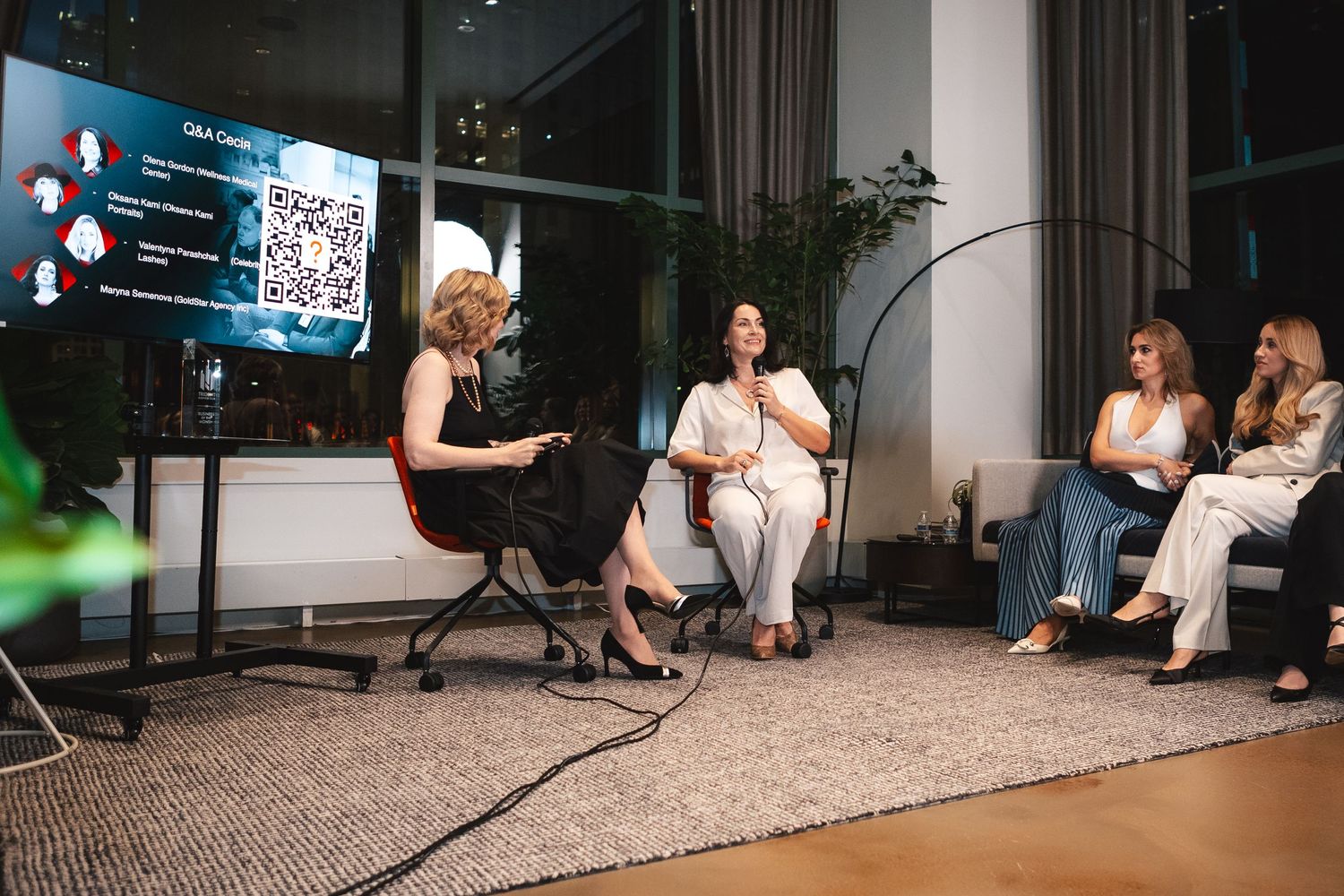 Professional presentation with speakers and audience members in a modern office space with QR code display.