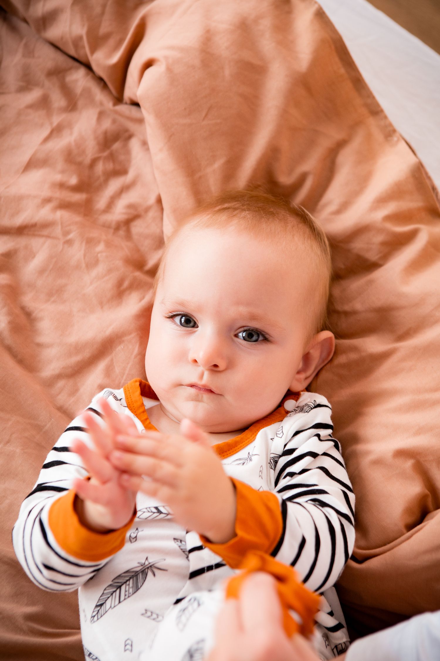 Baby wearing striped shirt lying on peach-colored fabric.