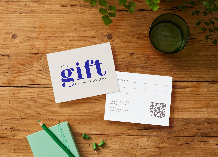 Green stationery and business cards arranged on wooden desk surface with scattered decorative vine leaves.