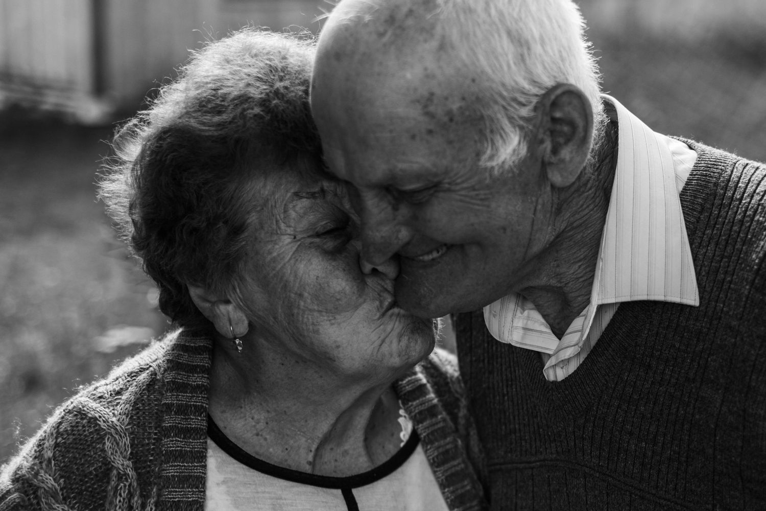 An intimate black and white portrait of an elderly couple sharing a tender moment.