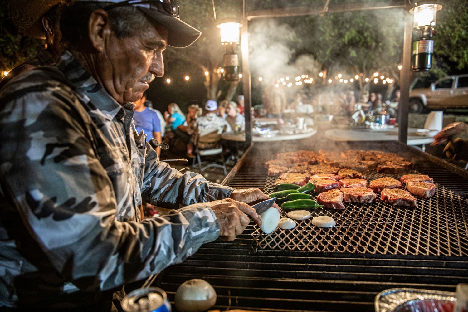 Man flipping steaks over a large fire
