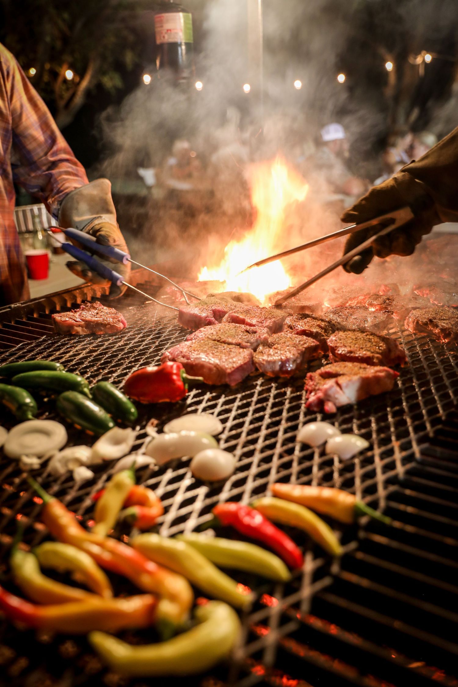 Man flipping steaks over a large fire