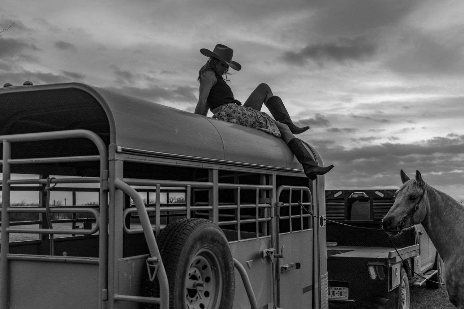 Girl sitting on top of a trailer with a cowboy hat and horse