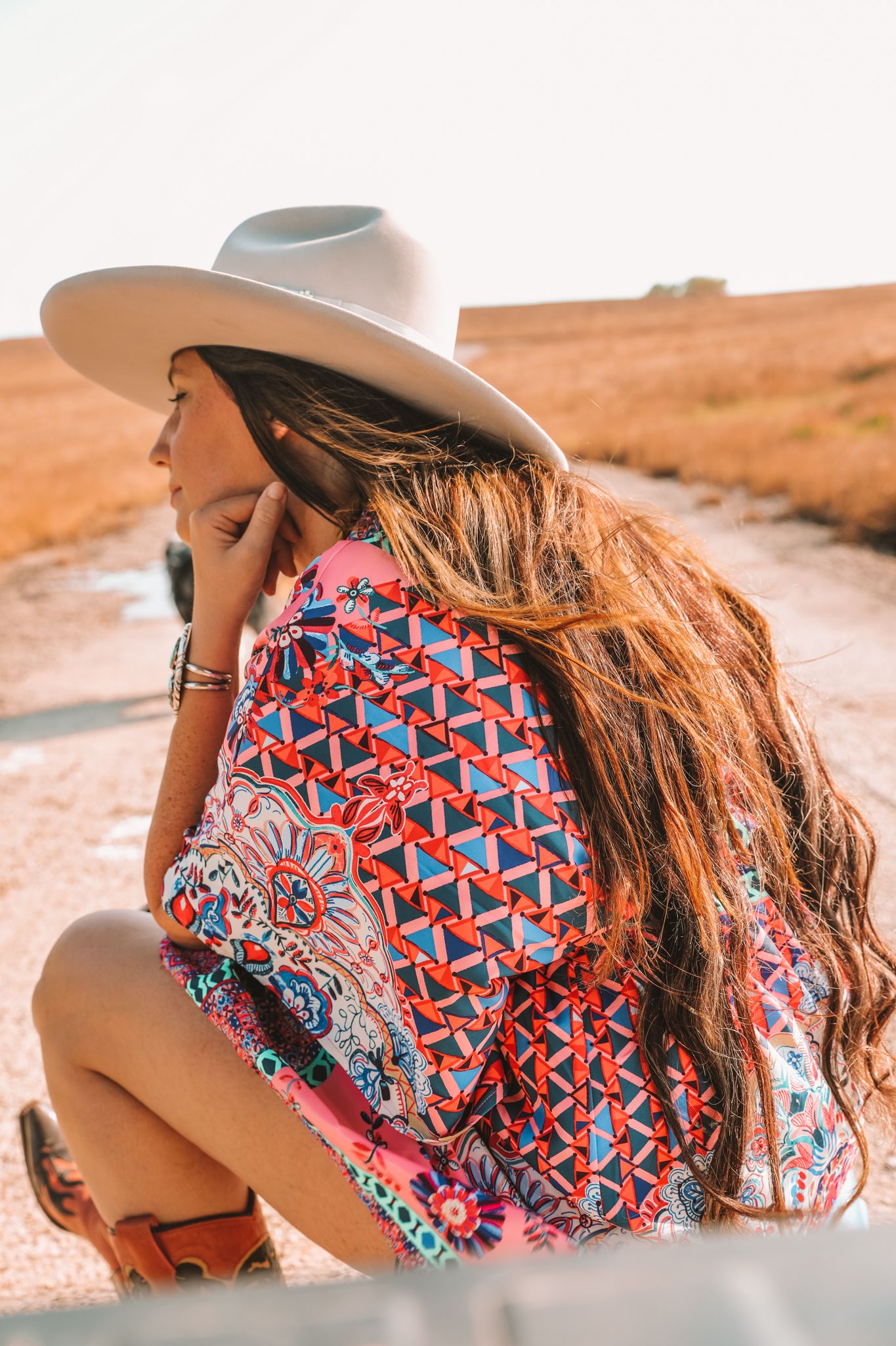 Woman sitting looking off in the distance wearing a silver cowboy hat a pink dress