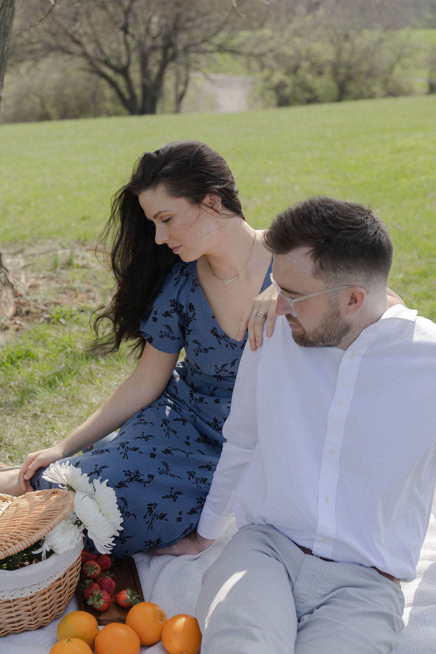 Couple enjoying a romantic outdoor picnic on a blanket with fresh fruits, strawberries, and flowers in a sunny park.
