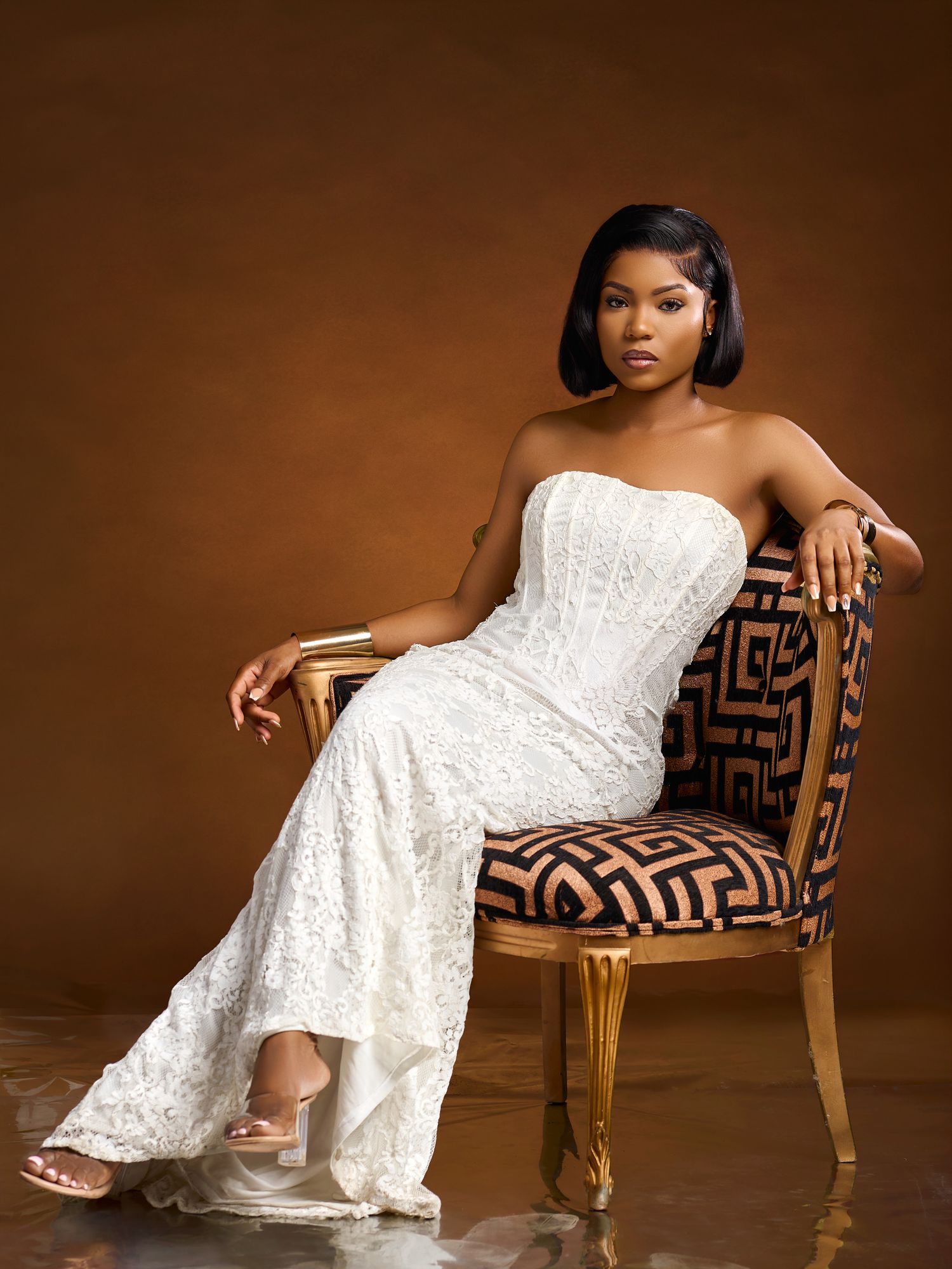 Elegant pose in white lace dress on patterned vintage chair.