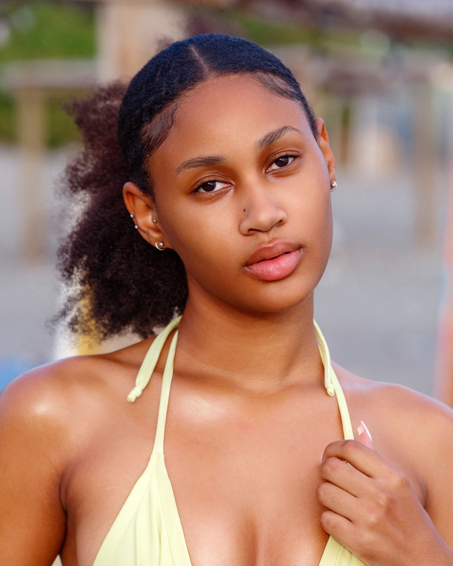 A model poses in casual outdoor setting wearing a yellow swimsuit with natural curly hair.
