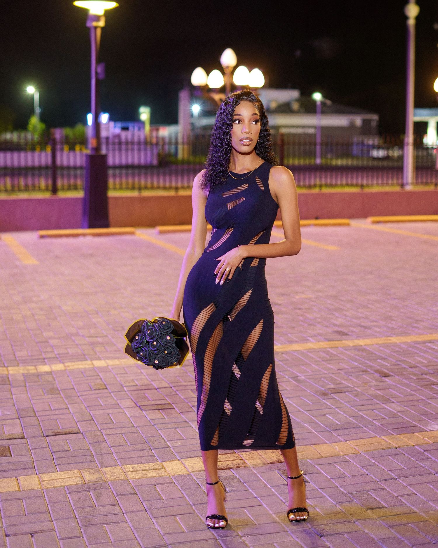 Fashion photoshoot at night featuring a navy blue dress on paved courtyard.