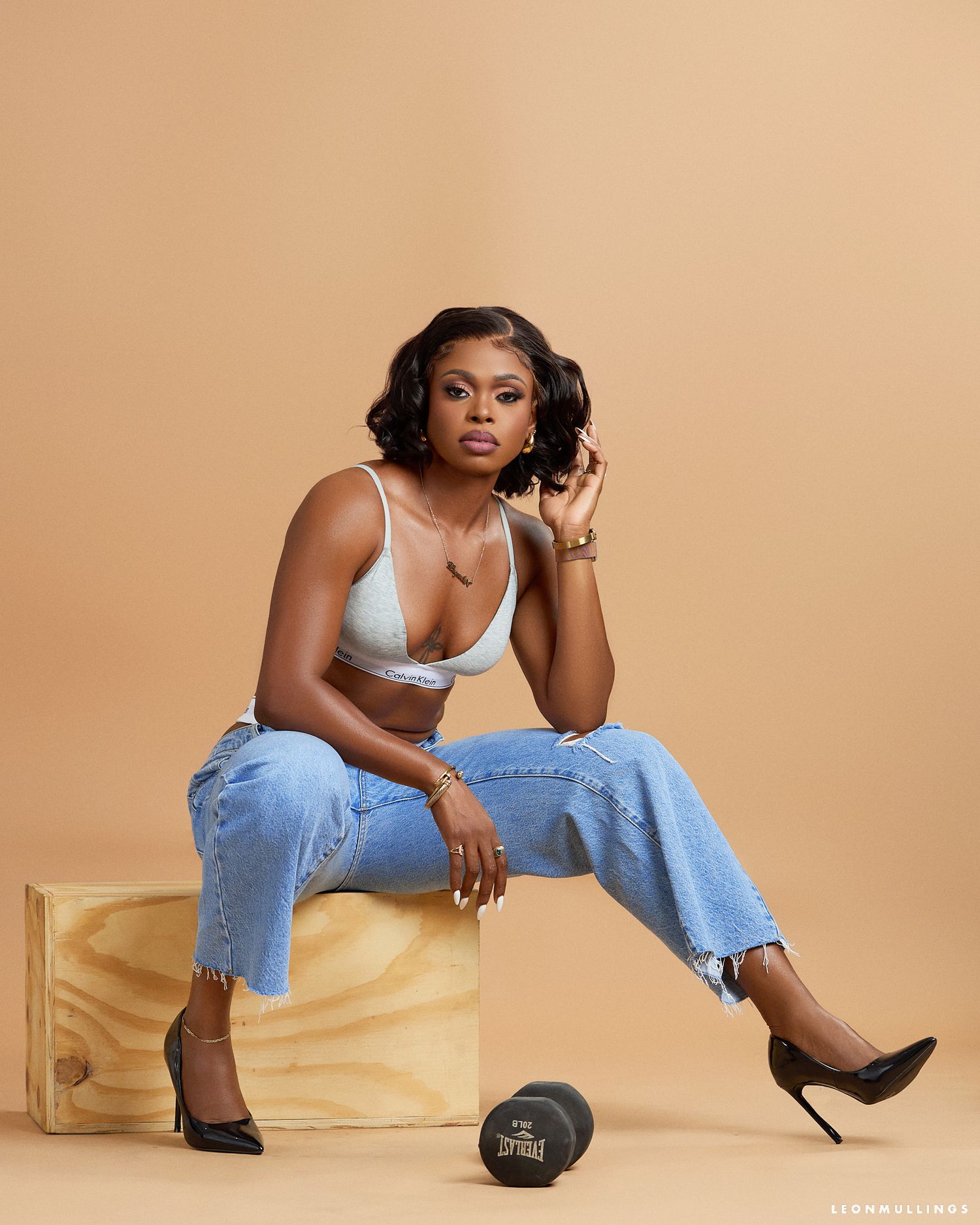 Stylish photoshoot featuring denim and white lingerie with wooden prop and beige backdrop.