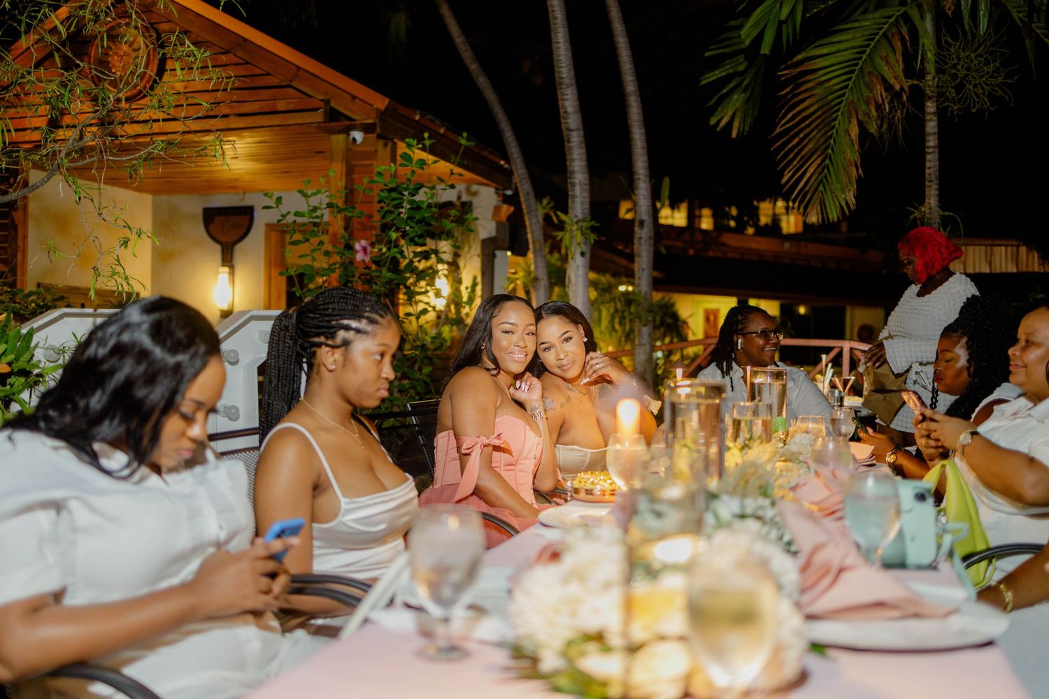 Candlelit outdoor dinner party with friends gathered around tables.