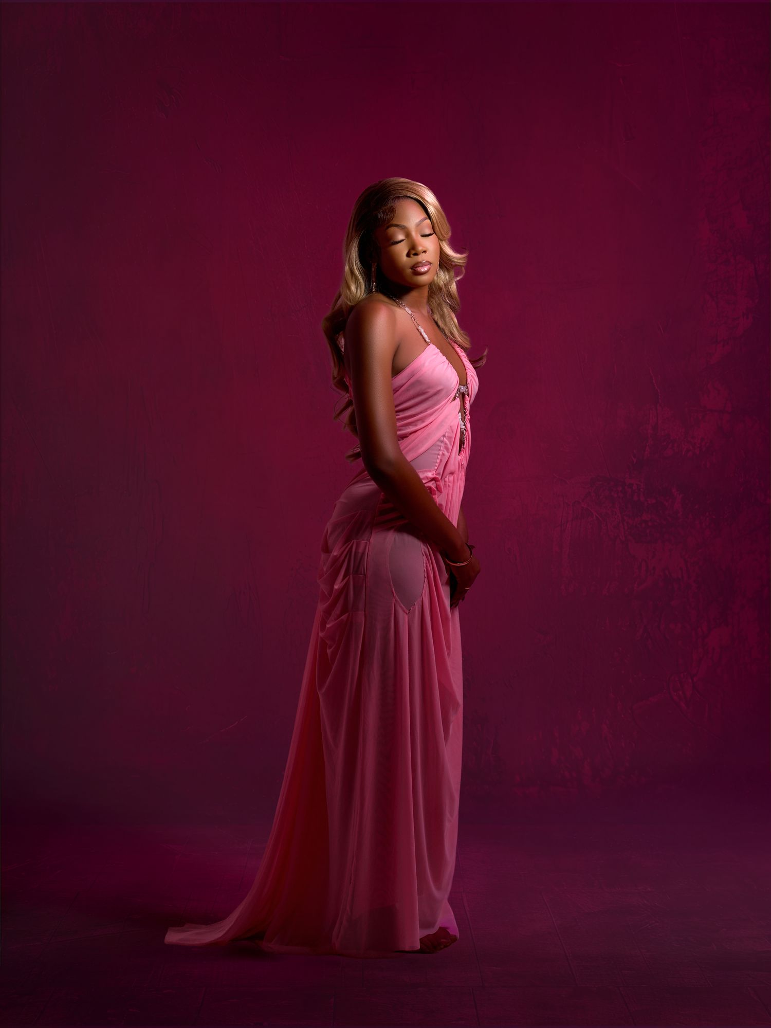 Elegant pose in flowing pink gown against burgundy studio backdrop.