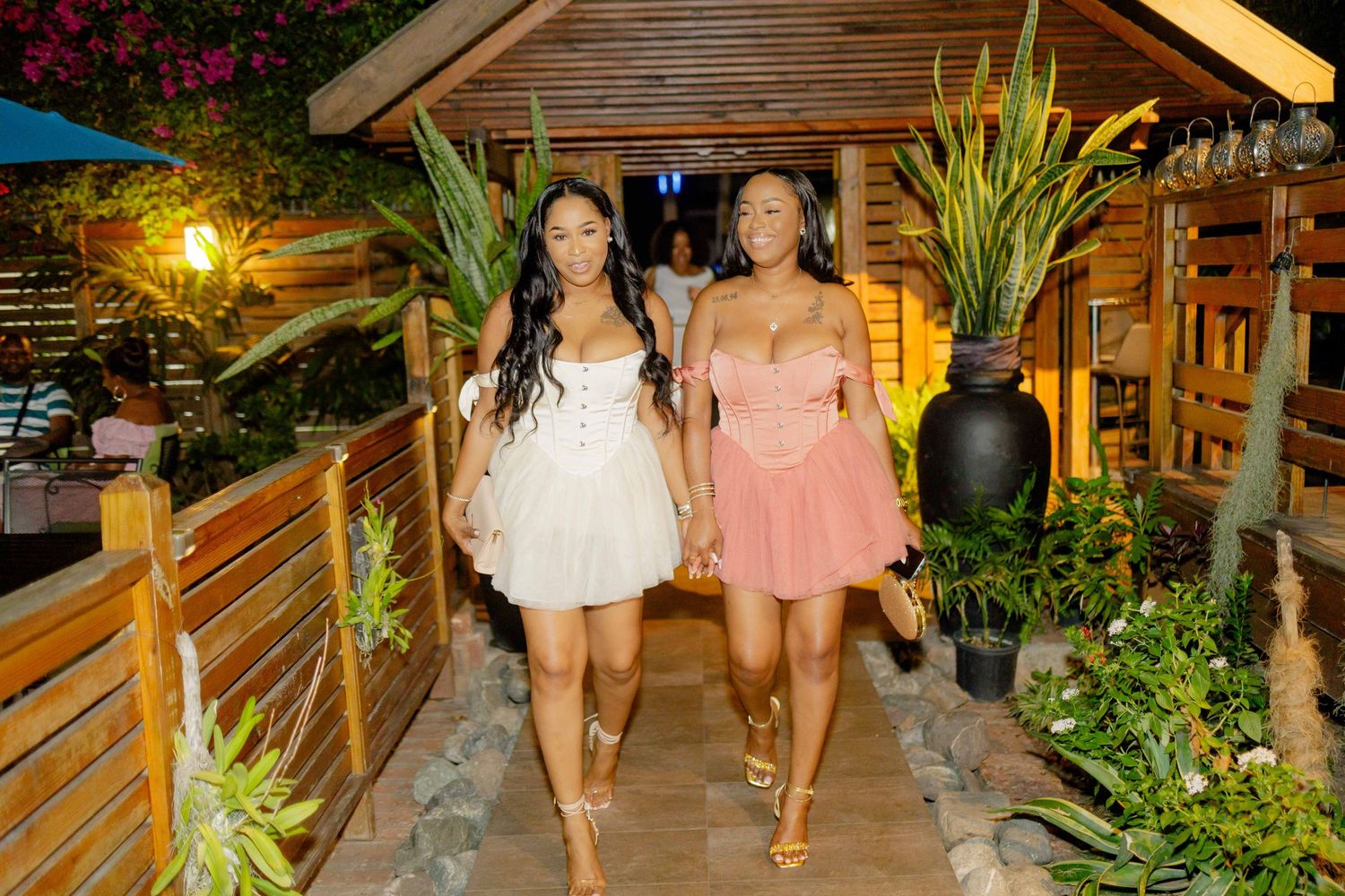 Group walking through tropical garden path with wooden structures at night.