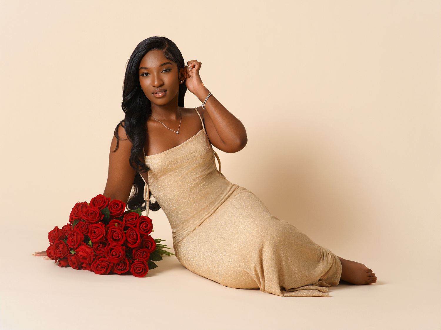 Elegant maternity photoshoot with beige dress and red roses against light background.