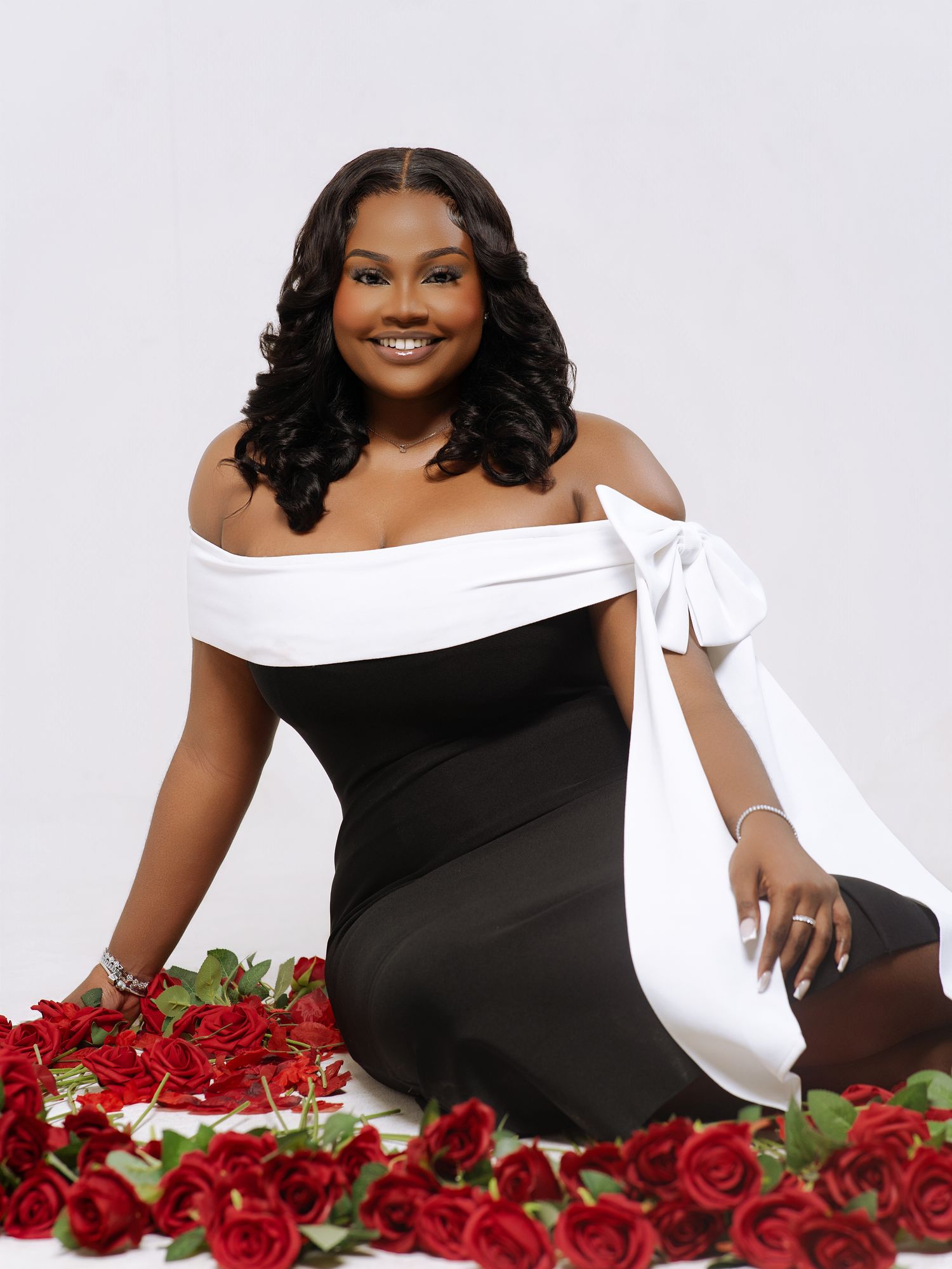 Glamour portrait with black and white outfit surrounded by red roses on white background.
