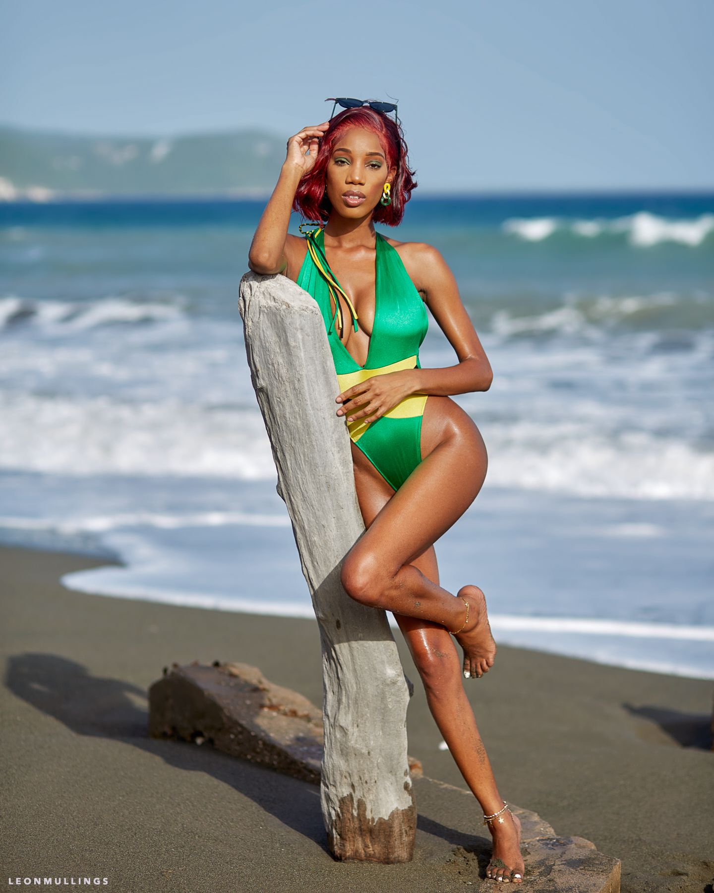 Beach photoshoot featuring green and yellow one-piece swimwear against ocean backdrop.