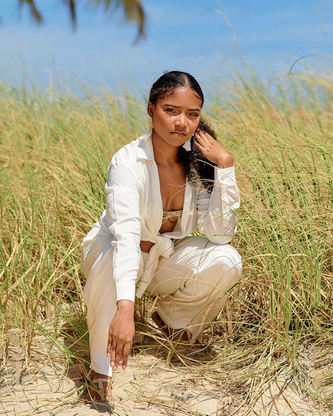 Model poses in white outfit among beach grass during golden hour.