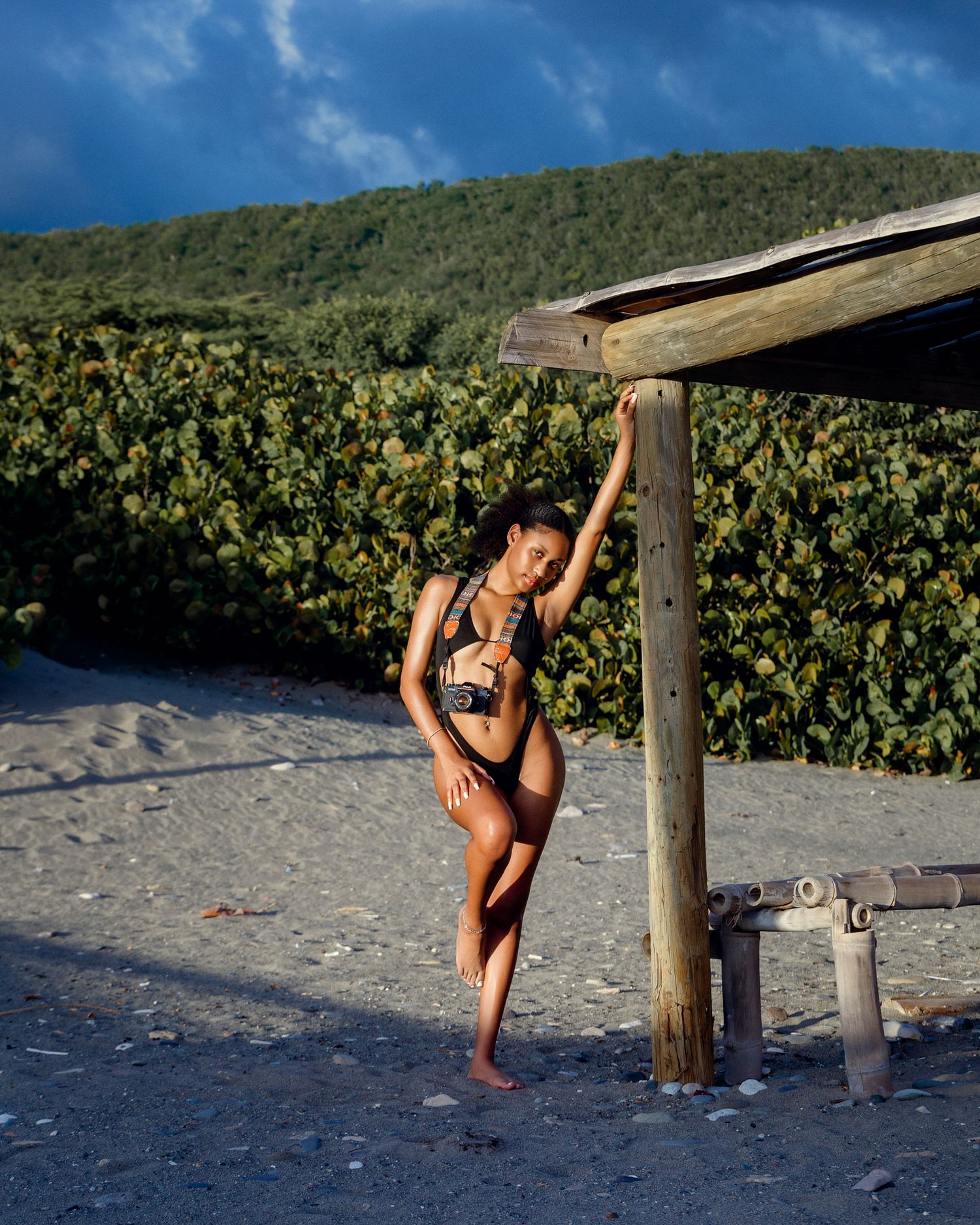 Beach photography scene with wooden posts and tropical greenery in background.