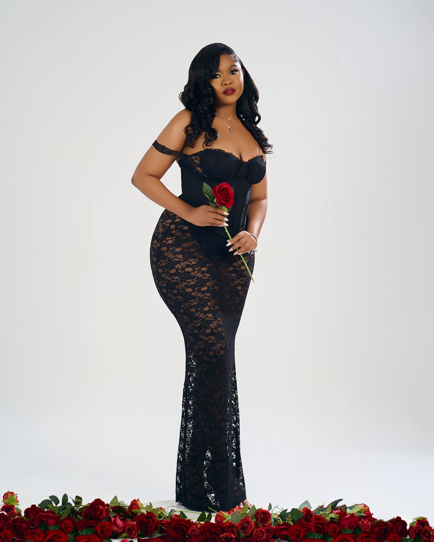 Beautiful black lace gown photoshoot with red roses and white backdrop.
