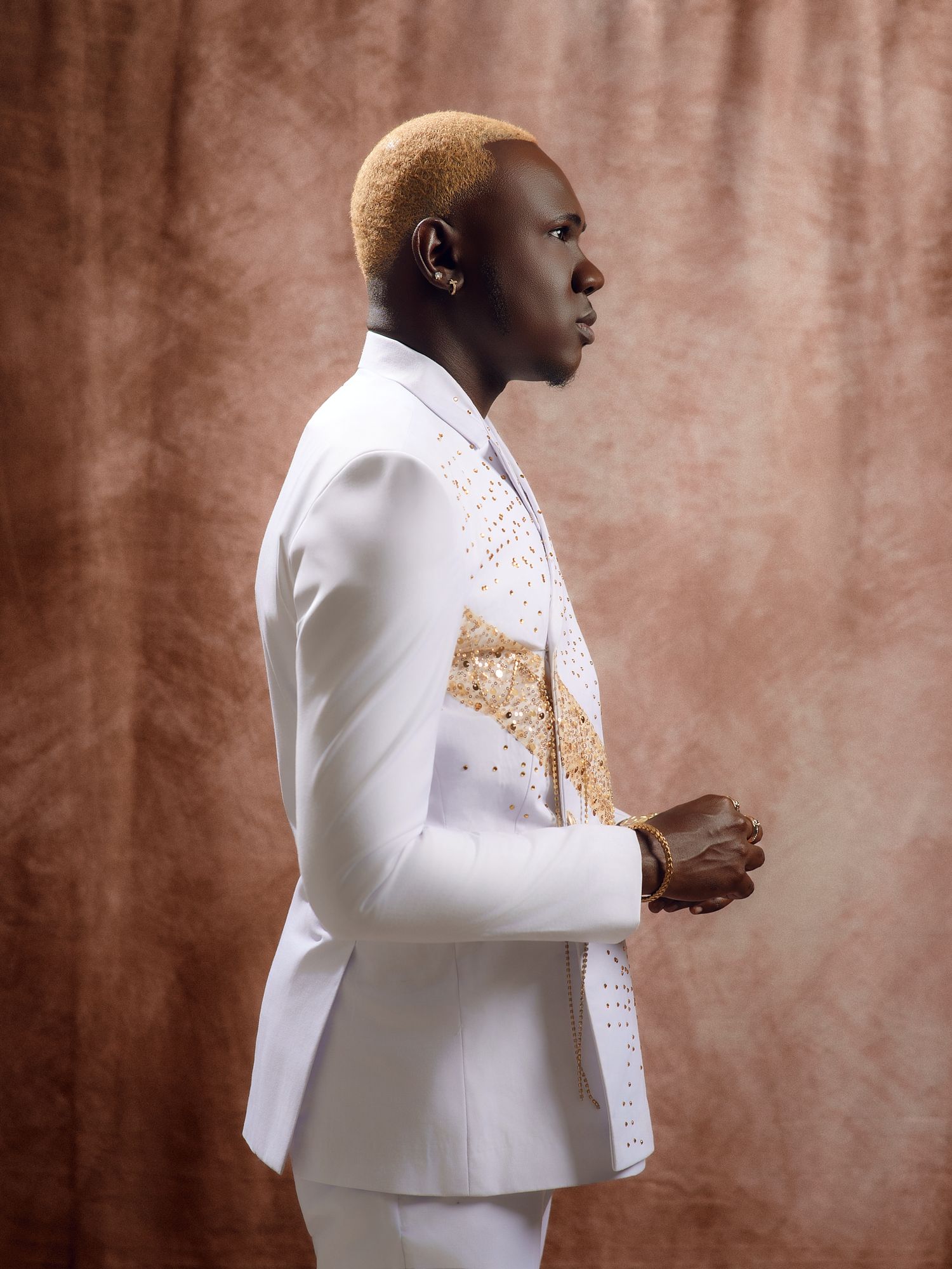Fashion portrait series in crisp white suit against textured brown backdrop.