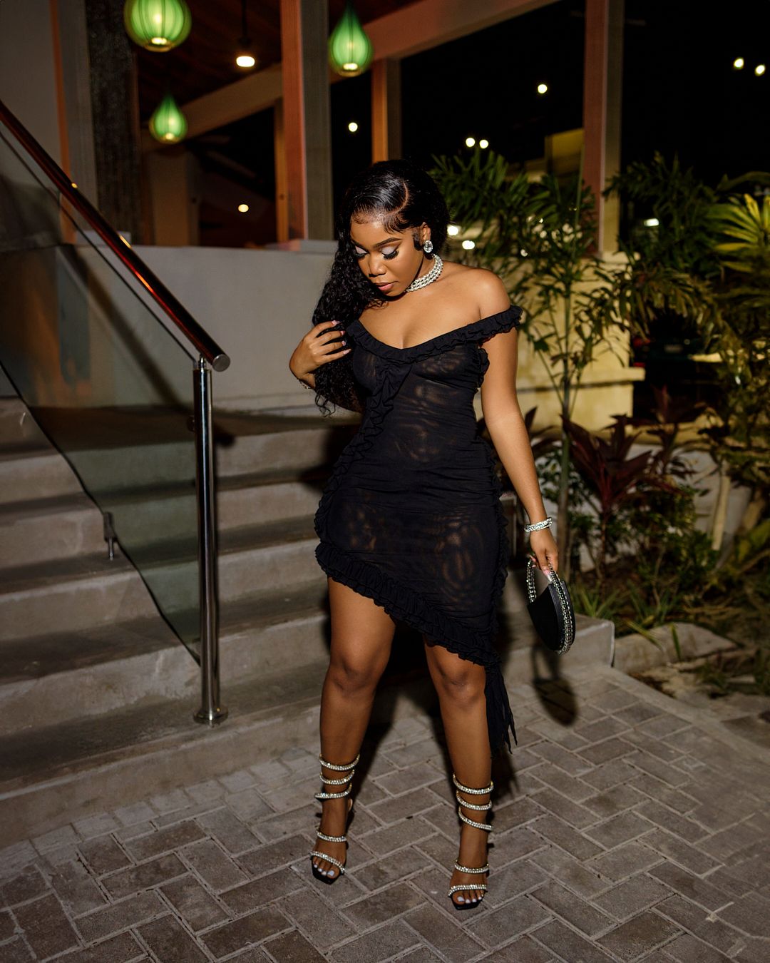 Fashion pose on stone steps showcasing strappy heels and a black dress.