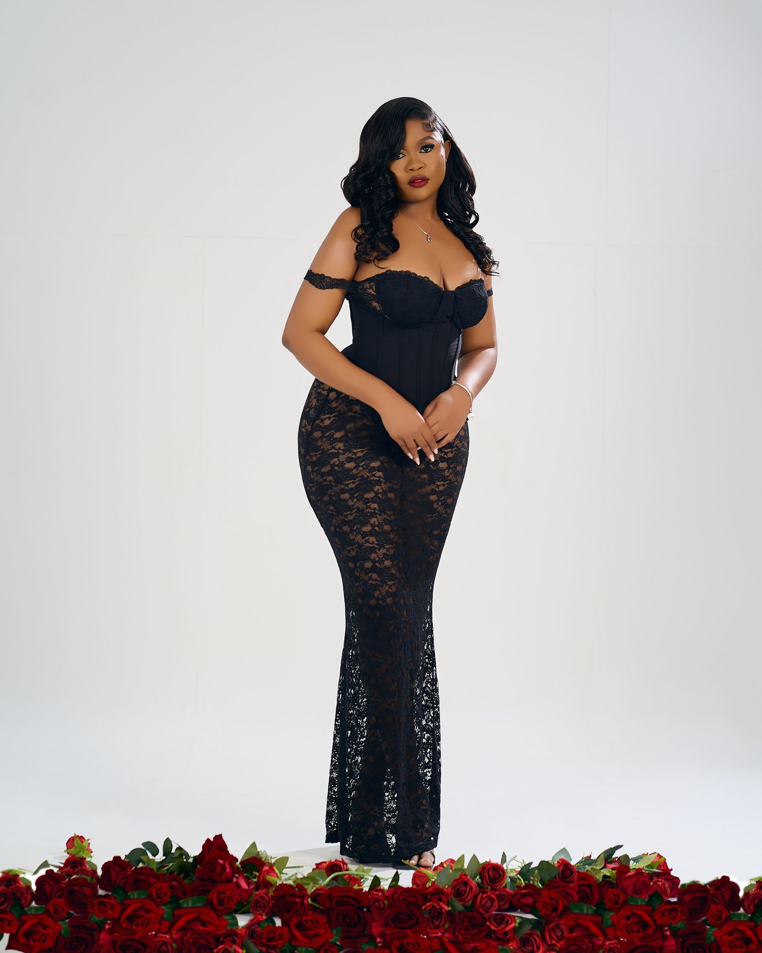 Full-length shot of black lace gown with red rose border against white background.