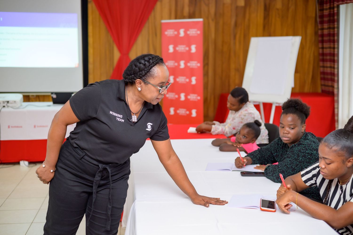 A trainer leans over a table assisting participants taking notes during a professional workshop seminar.
