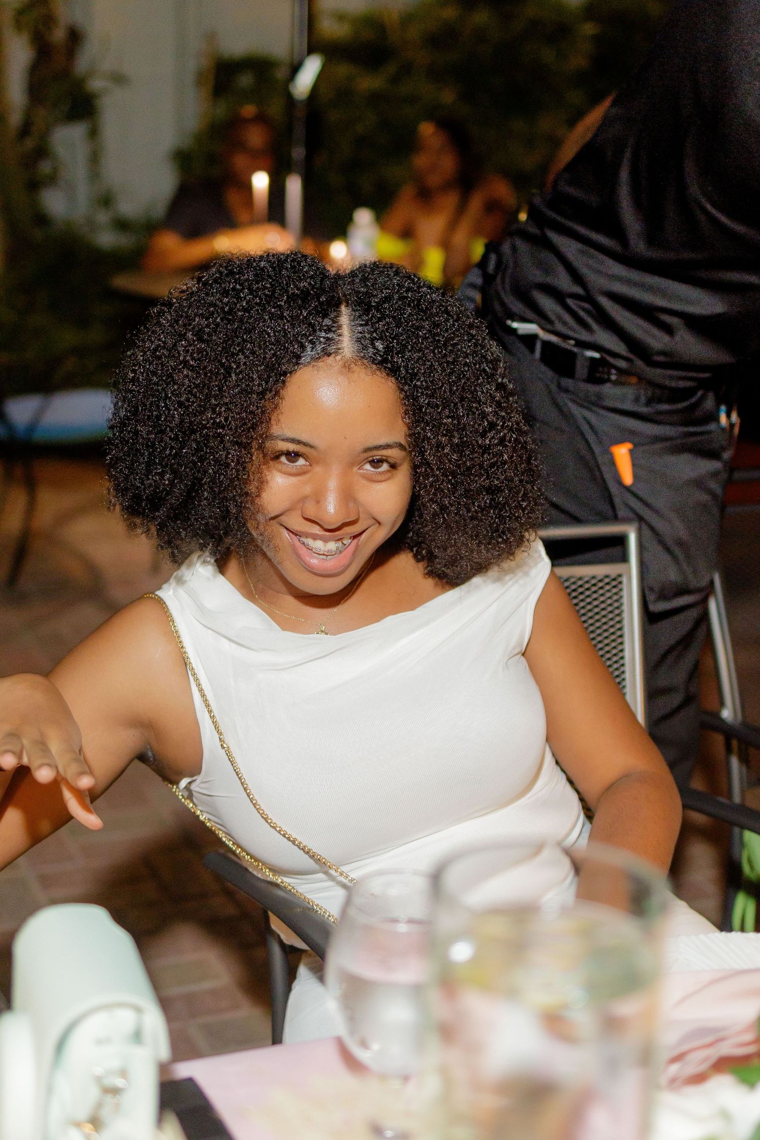 Person in white top smiling at dinner table with natural curly hair.