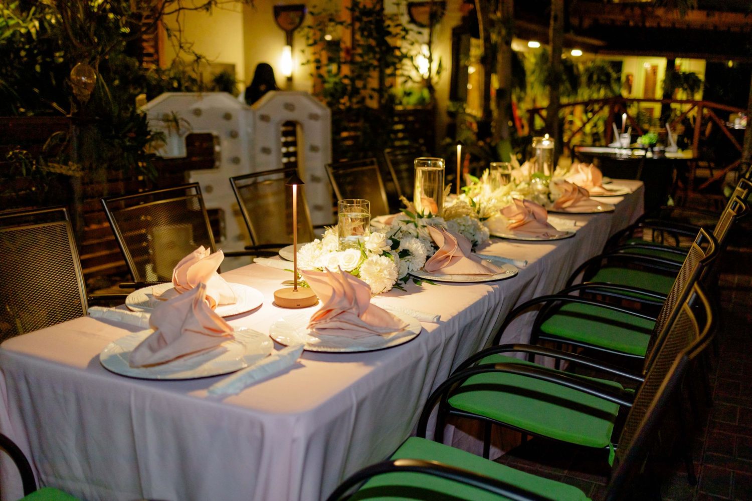 Elegant dinner table setup with white linens and green chairs in restaurant.
