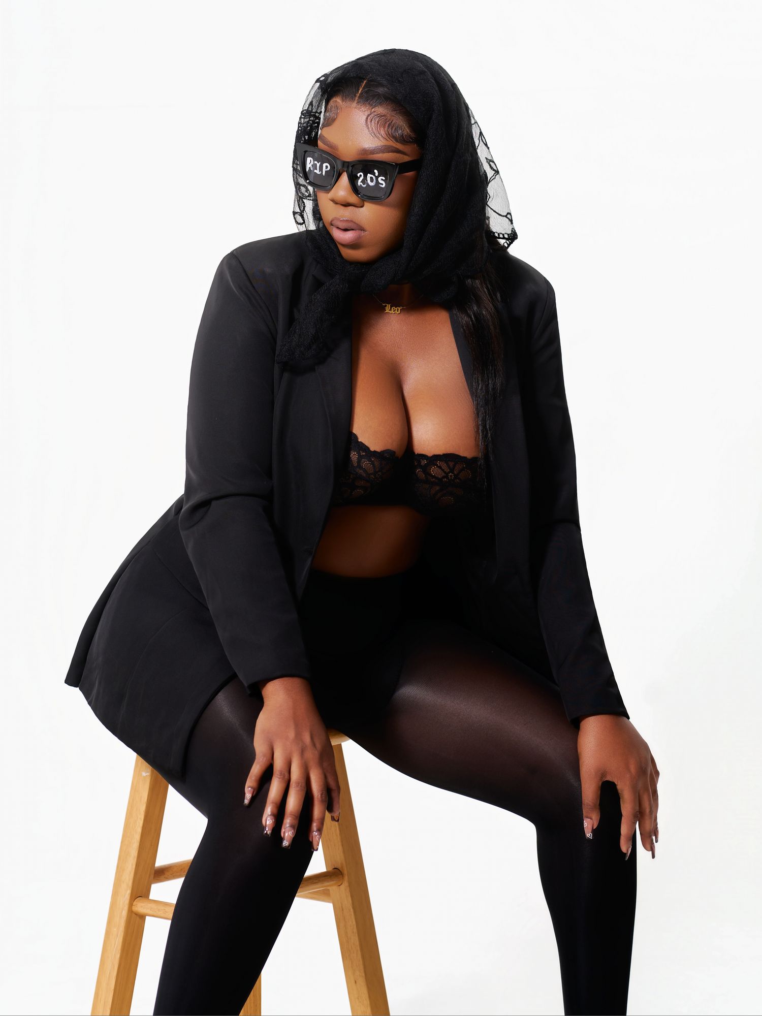 Professional studio photos featuring black blazer outfit with sunglasses on wooden stool.