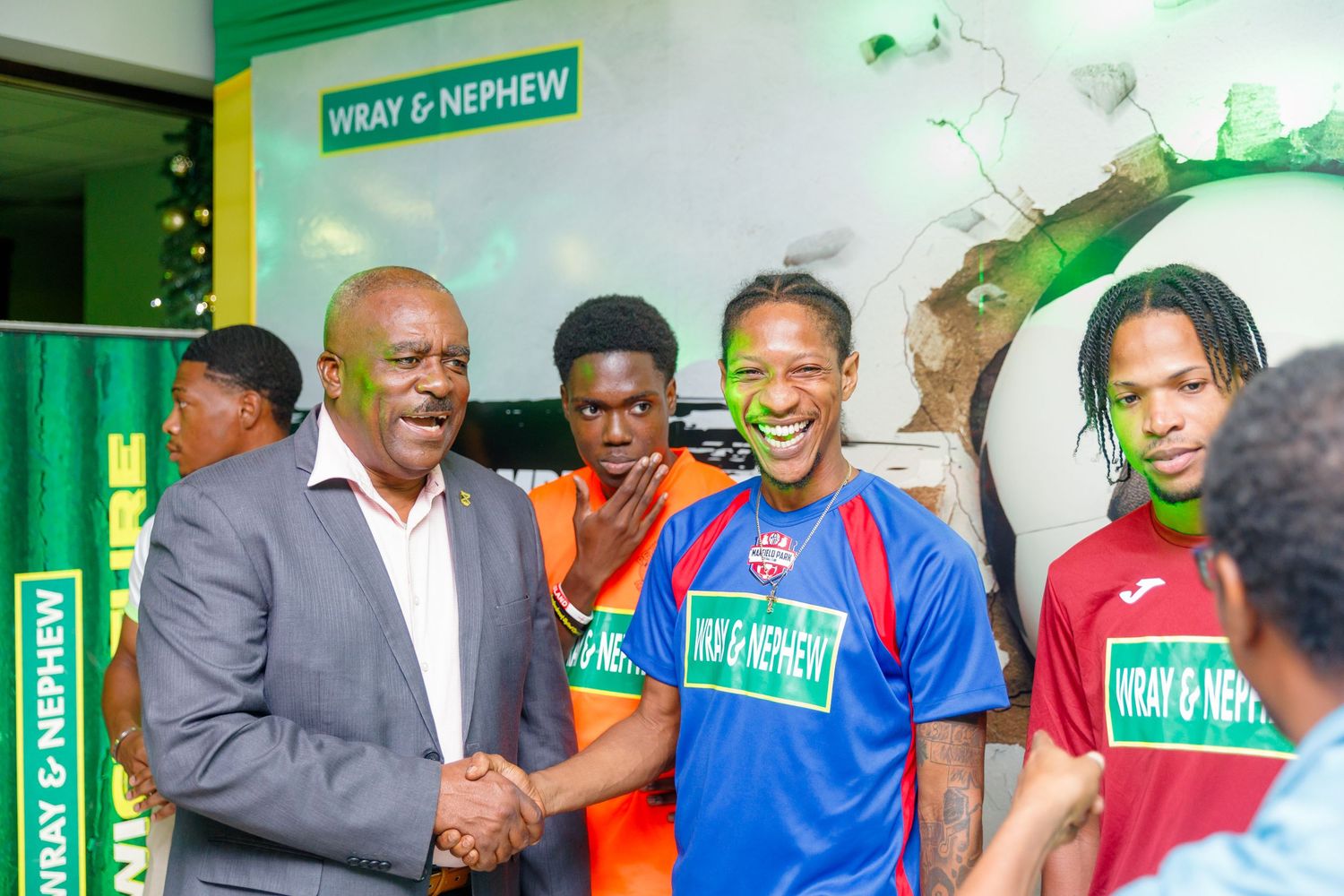 Men in Wray and Nephew branded jerseys shaking hands at a sponsored sports event indoors.