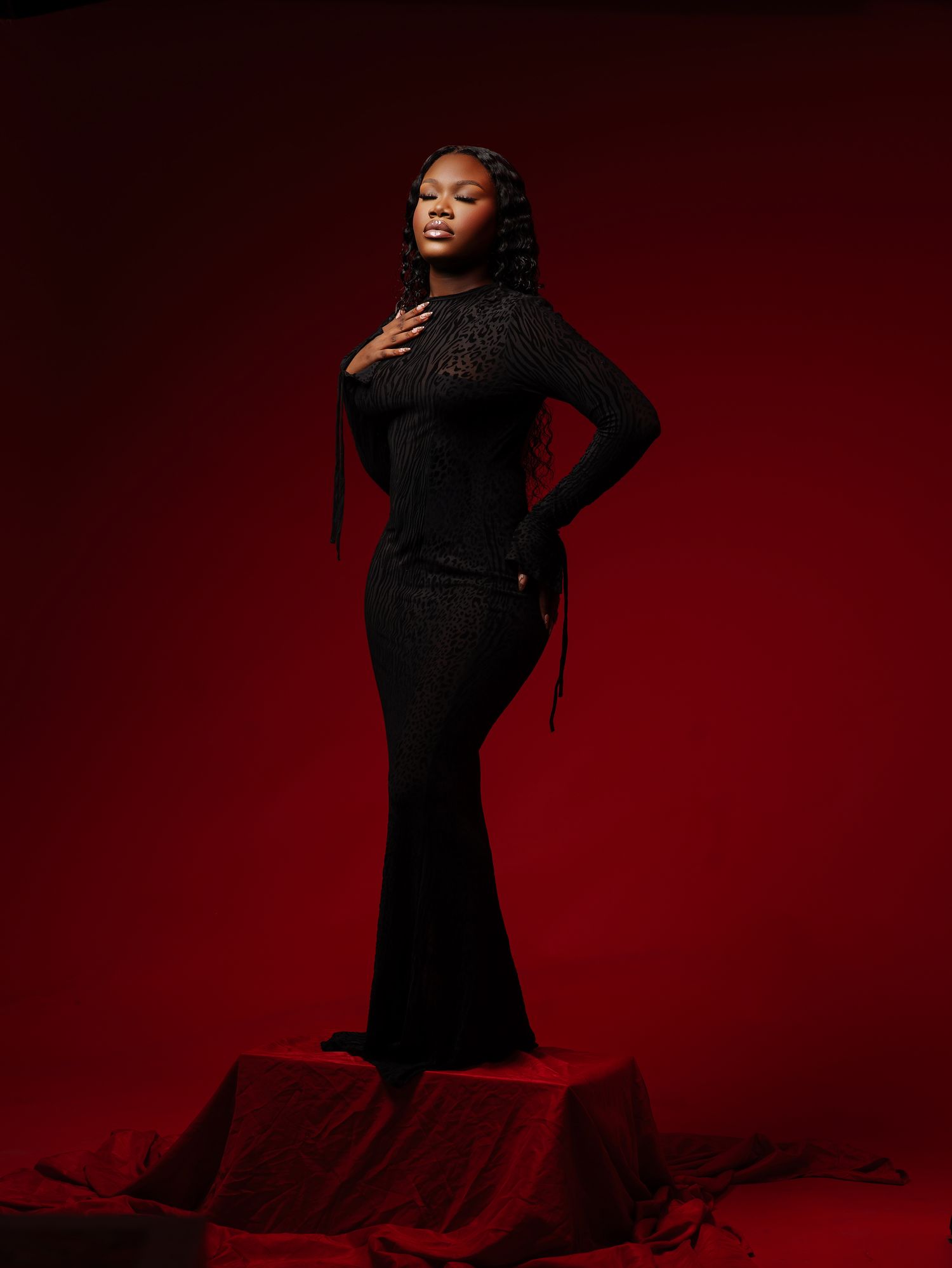 Dramatic fashion portrait in black dress against deep red background.