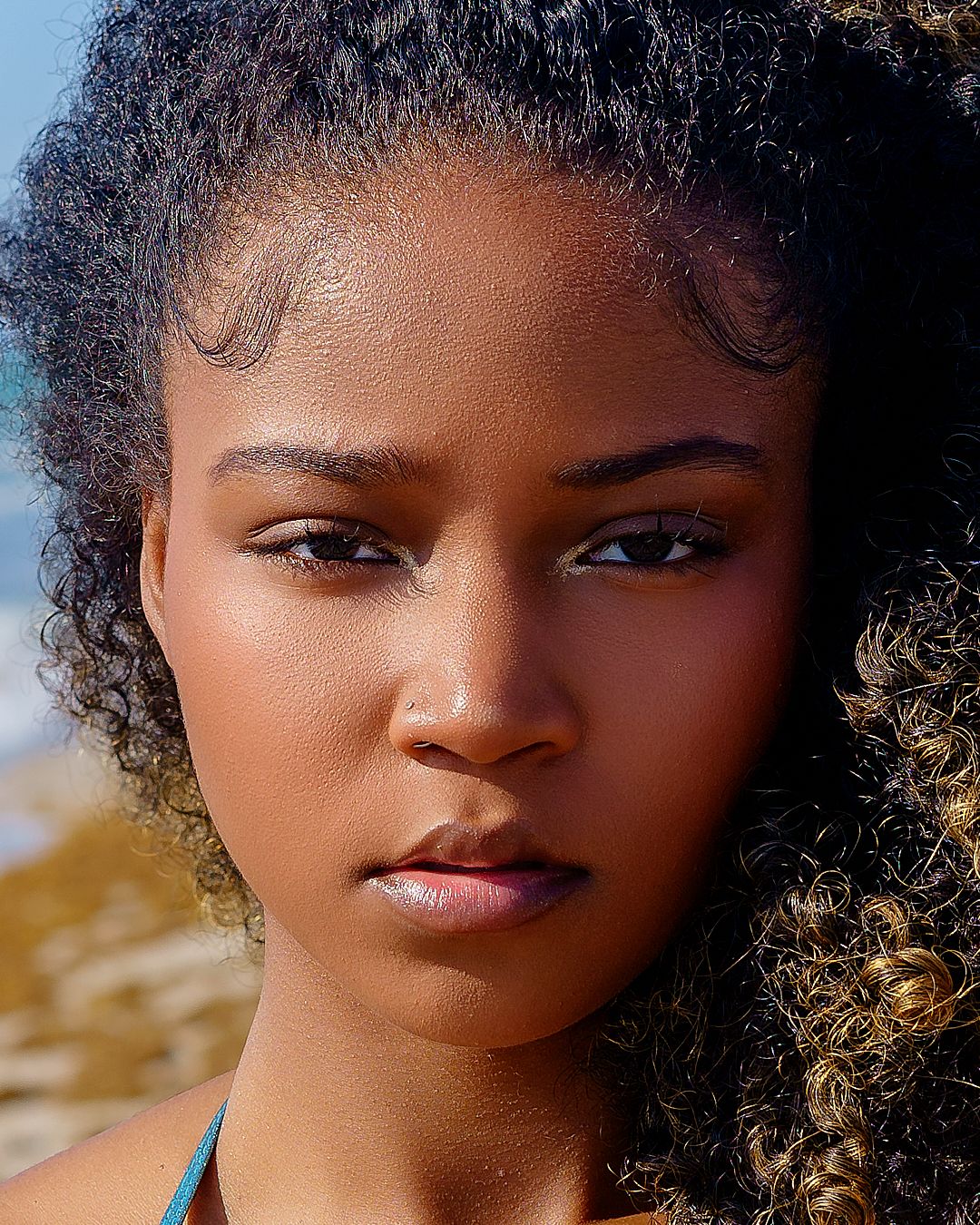 Close-up portrait with natural sunlight and beach backdrop.