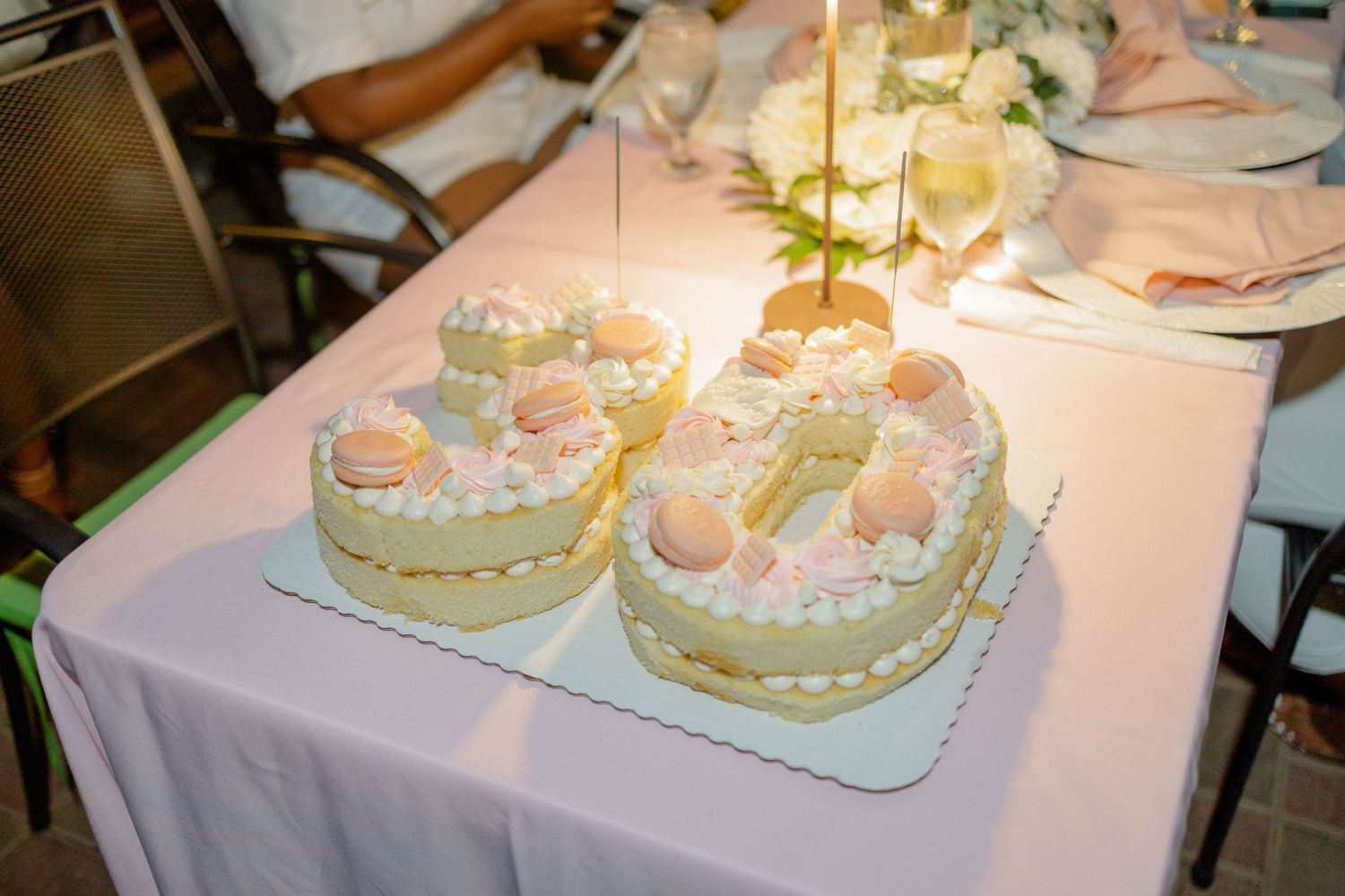 Birthday cake with lit candles on white tablecloth at outdoor celebration.