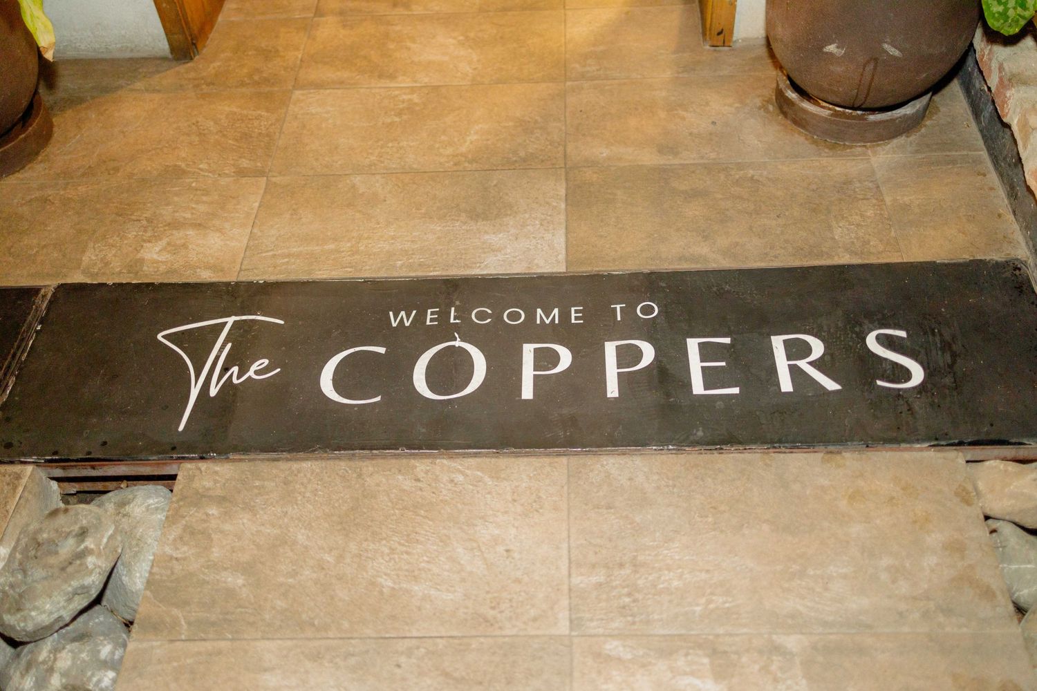 Welcome to Coppers sign displayed on wooden floor in restaurant entrance.