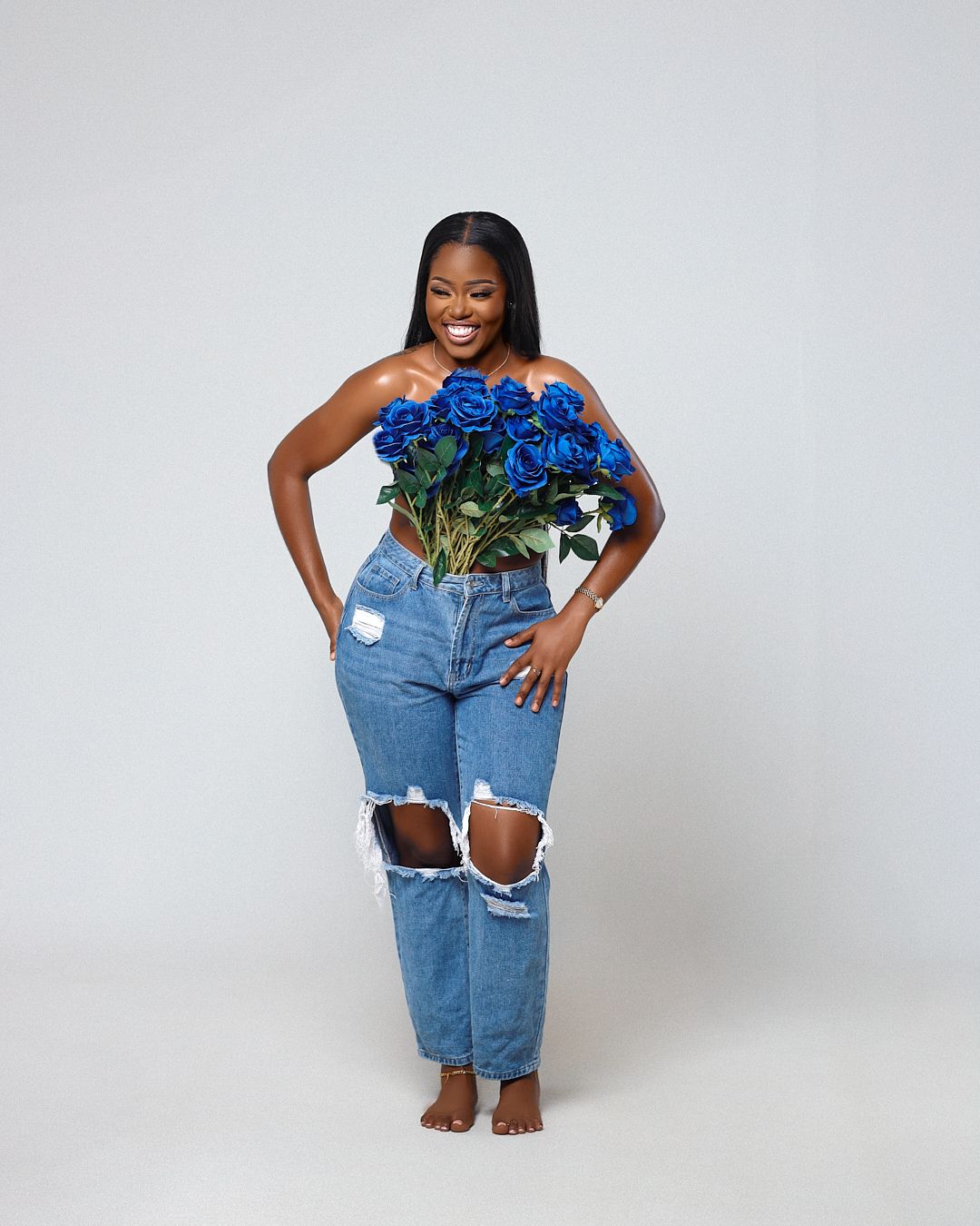 A person wearing ripped blue denim jeans and a blue feathered top poses in four different positions against a white backdrop.