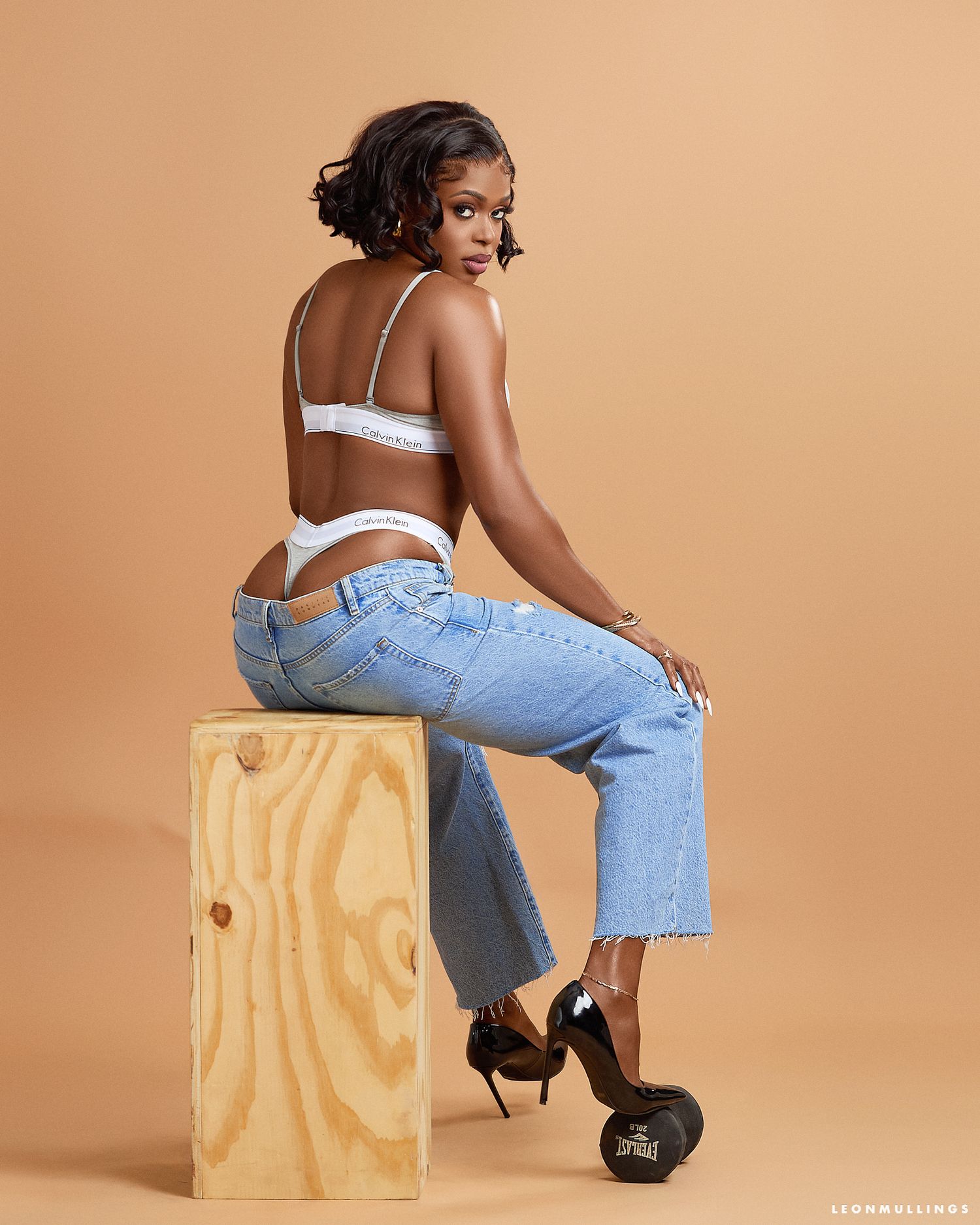 Fashion model strikes dynamic poses on wooden box wearing casual denim and heels.