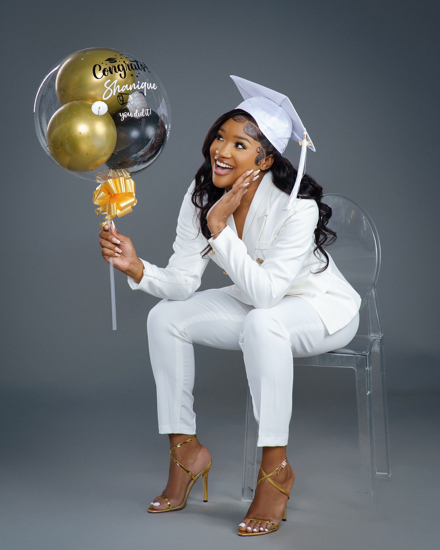 Glamorous studio photoshoot featuring a model in white outfit and brown boots posing with gold balloons.