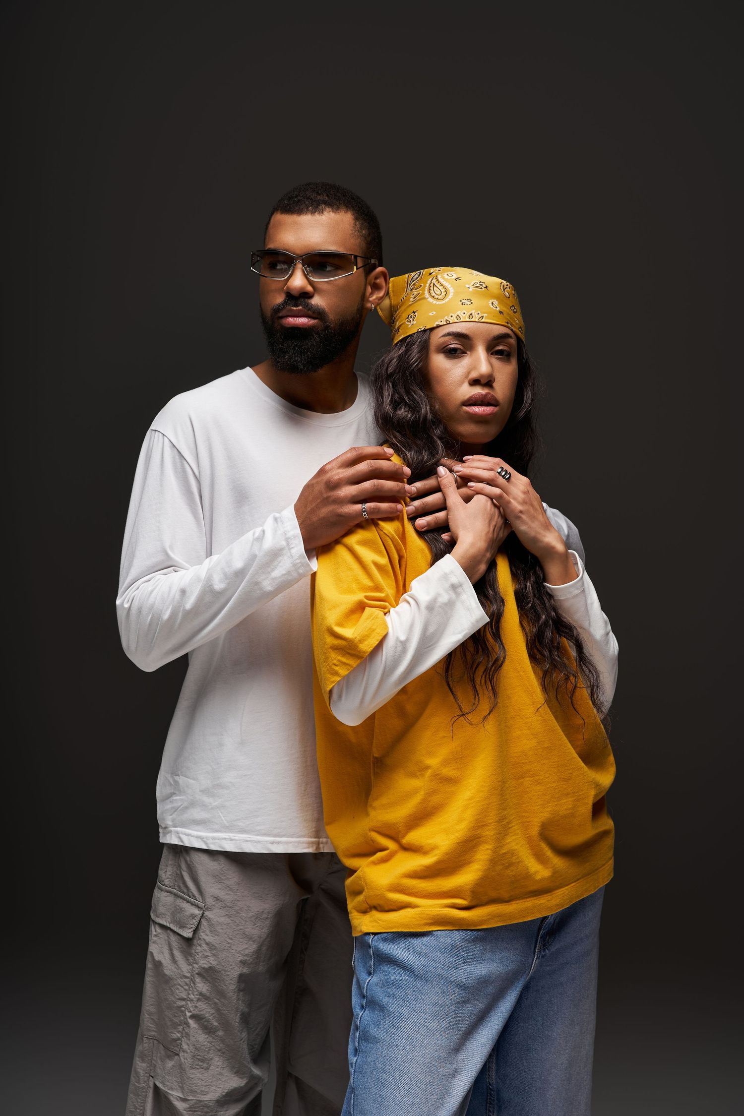 African American couple posing together, man in white long sleeve embracing woman in yellow hoodie.