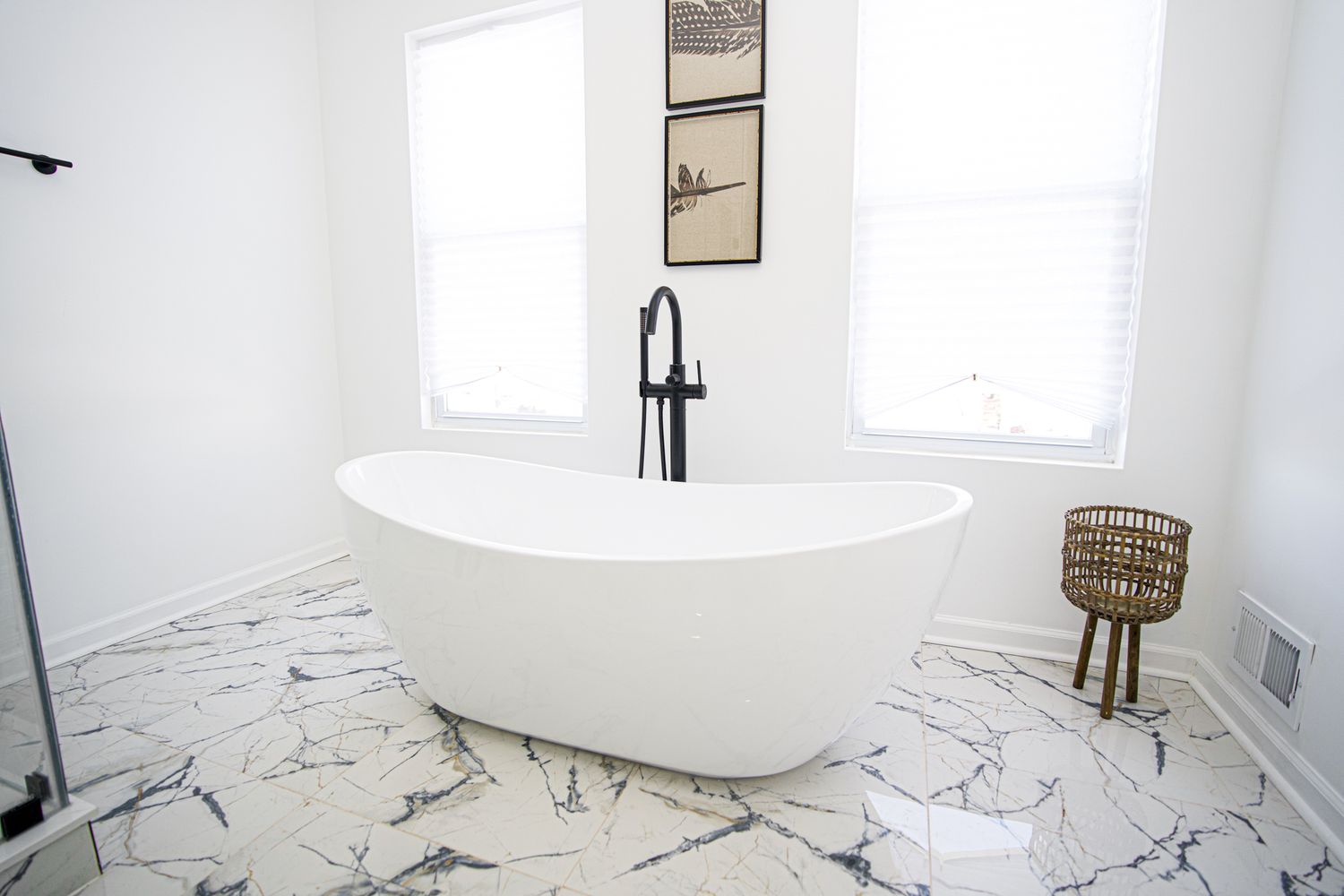 Modern white freestanding bathtub with matte black faucet on marble tile floor in bright minimalist bathroom.