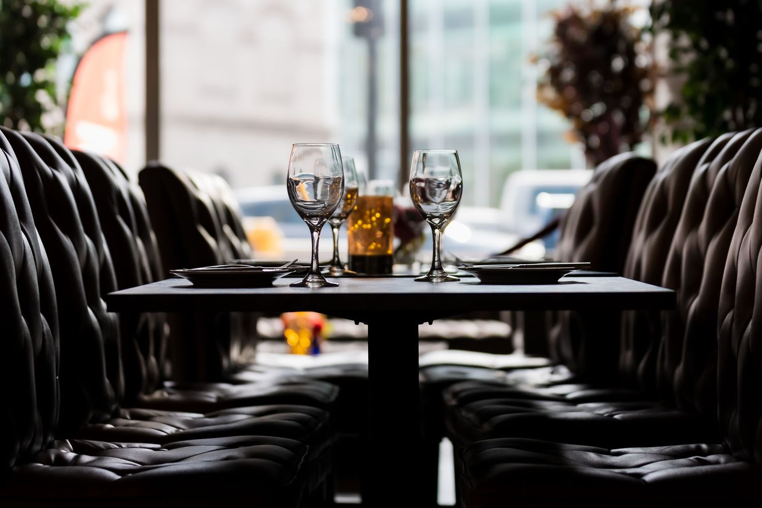 Elegant restaurant table set with wine glasses and candle centerpiece, surrounded by black leather chairs.