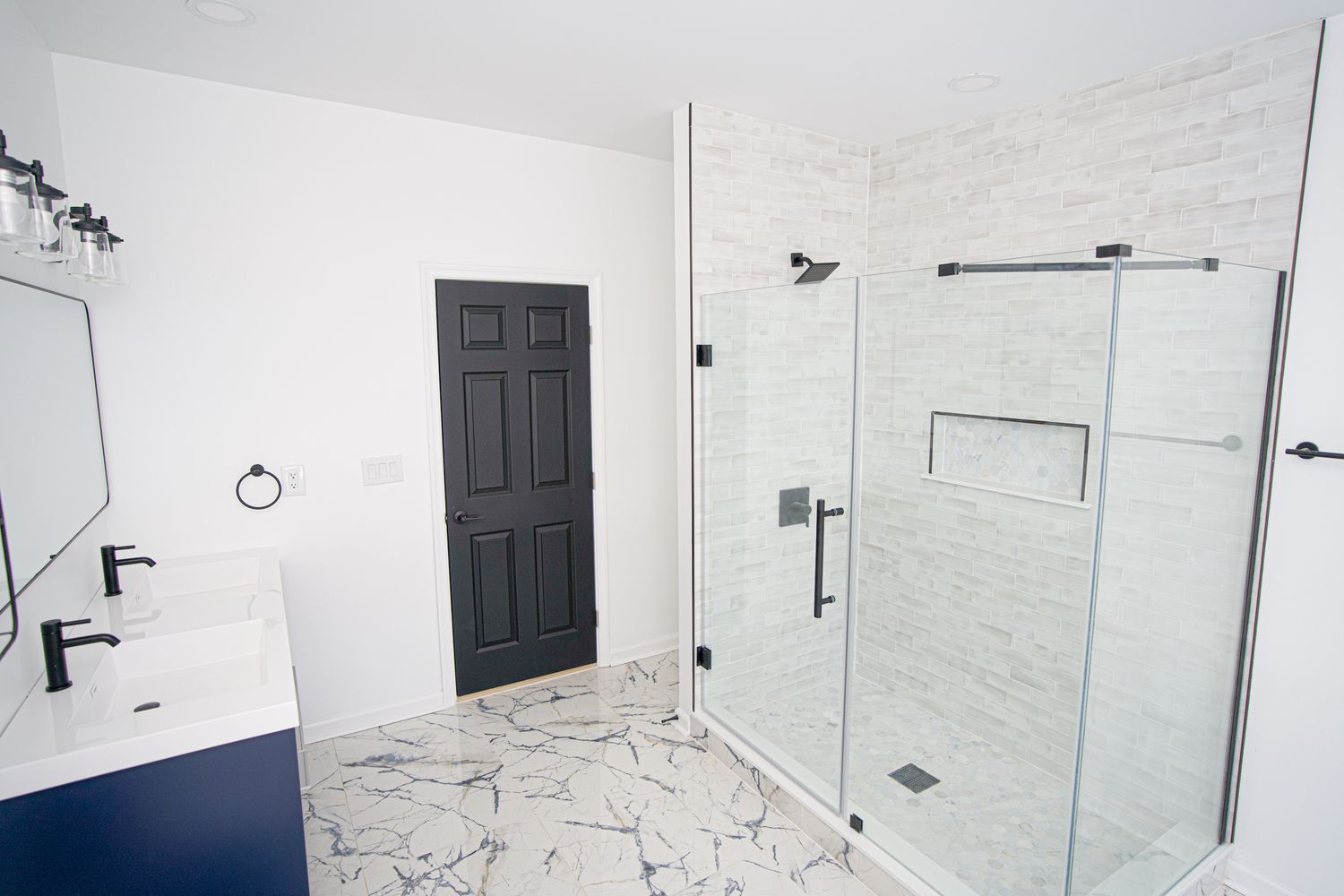 Modern bathroom with marble floors, glass shower, navy vanity, and black door accents.